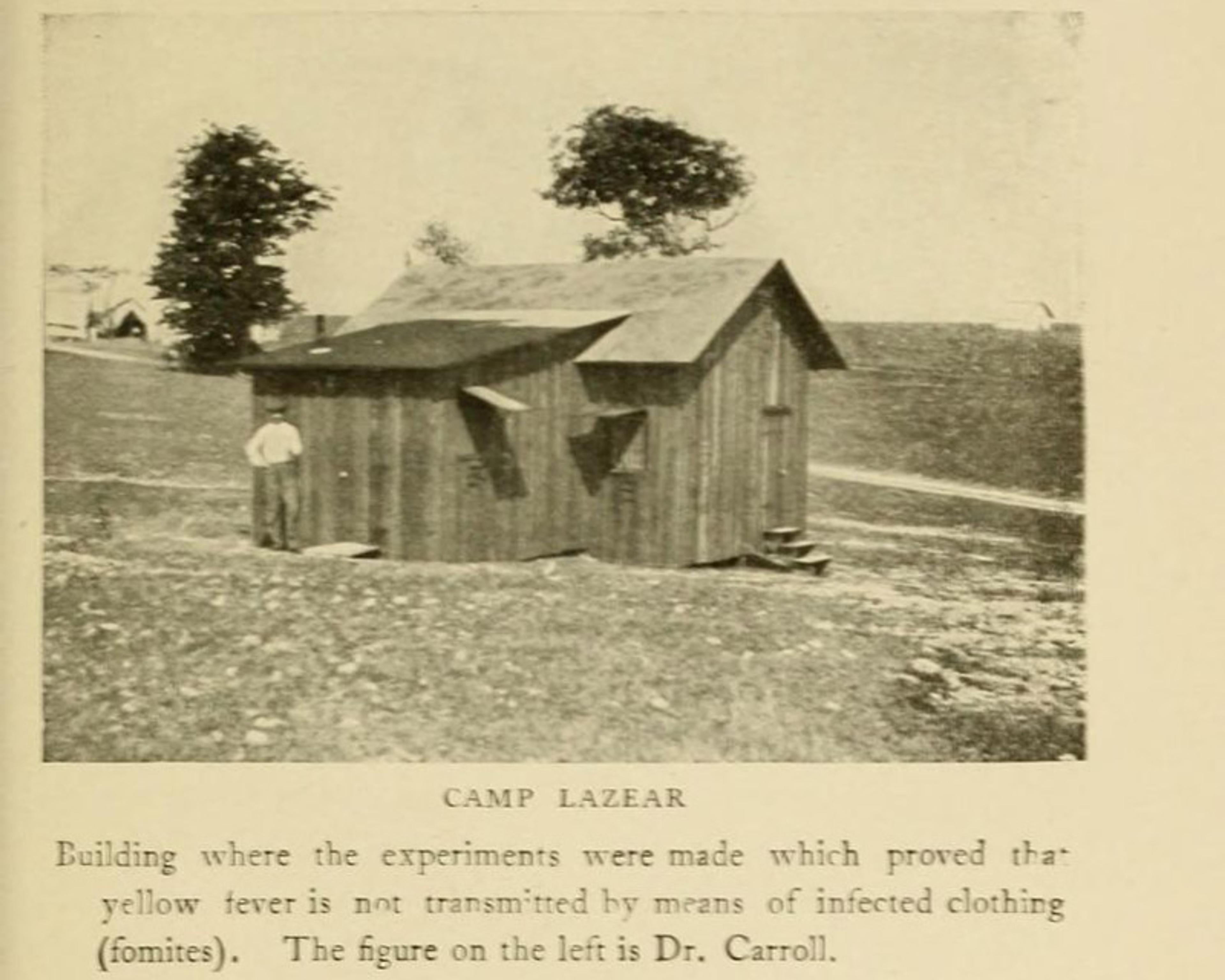 A sepia image of a man in 19th century shirt and trousers outside a small wooden hut