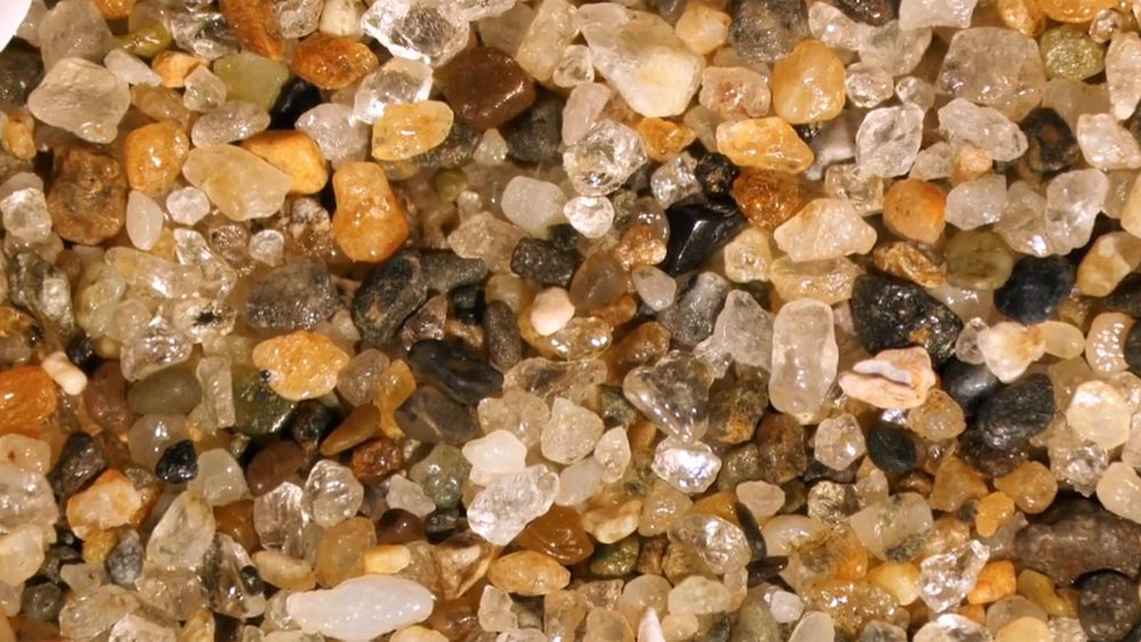 Close-up of variously coloured grains of sand including transparent, white, black and brown pebbles.