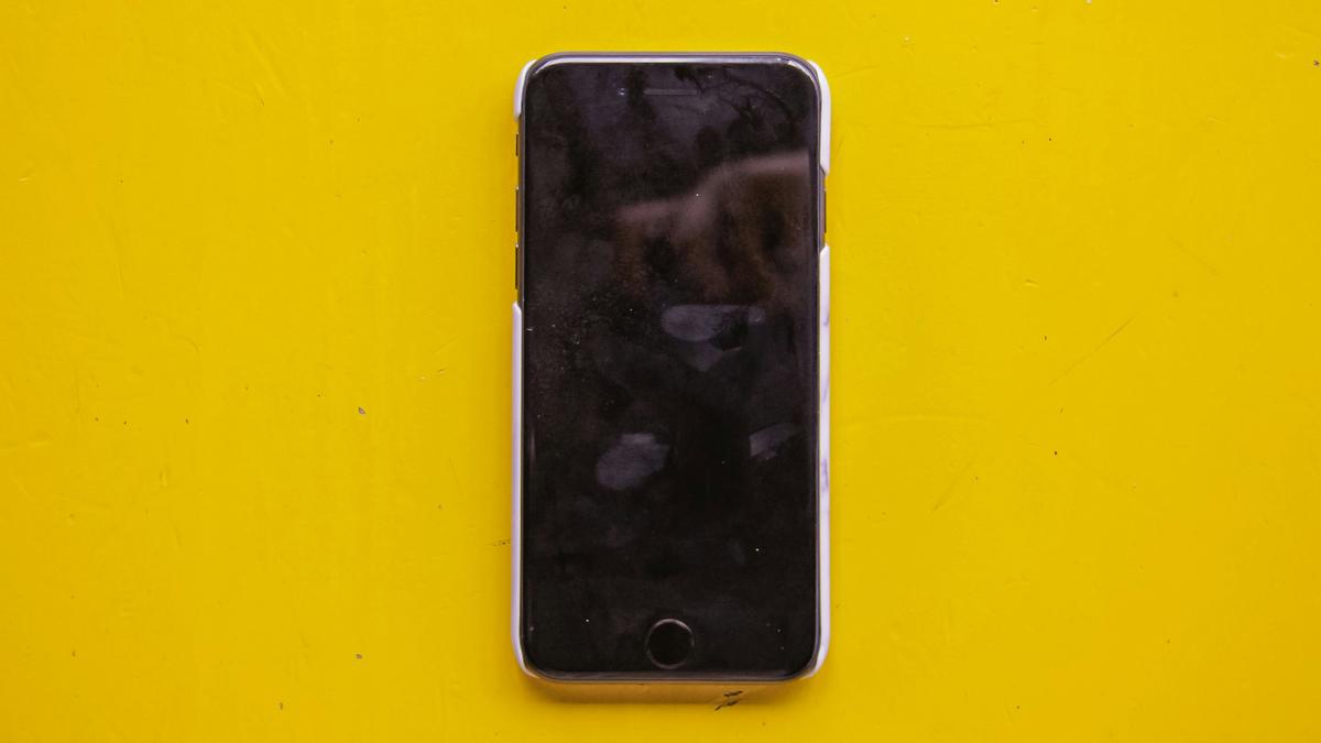 A switched-off smartphone on a bright yellow surface with fingerprints and smudges on the black screen.