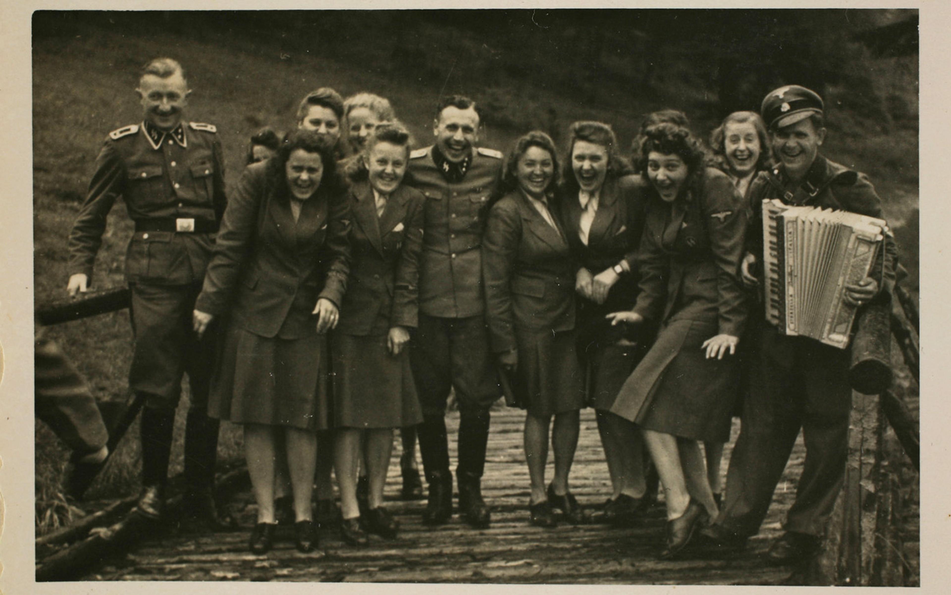 Vintage photo of uniformed women and men on a wooden bridge with one man playing an accordion, all appear to be laughing.