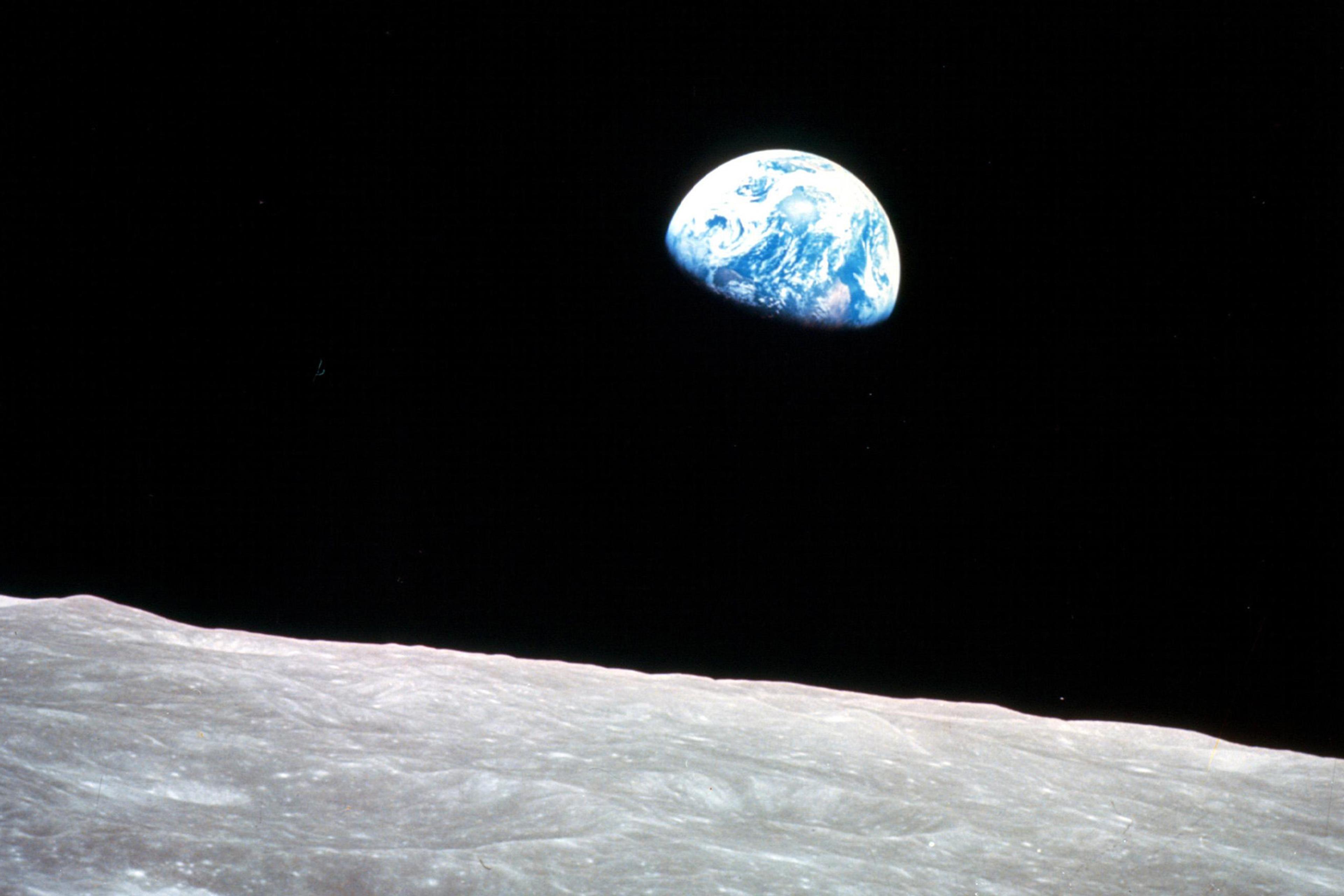 View of Earth, half visible, rising over the lunar surface against the blackness of space.