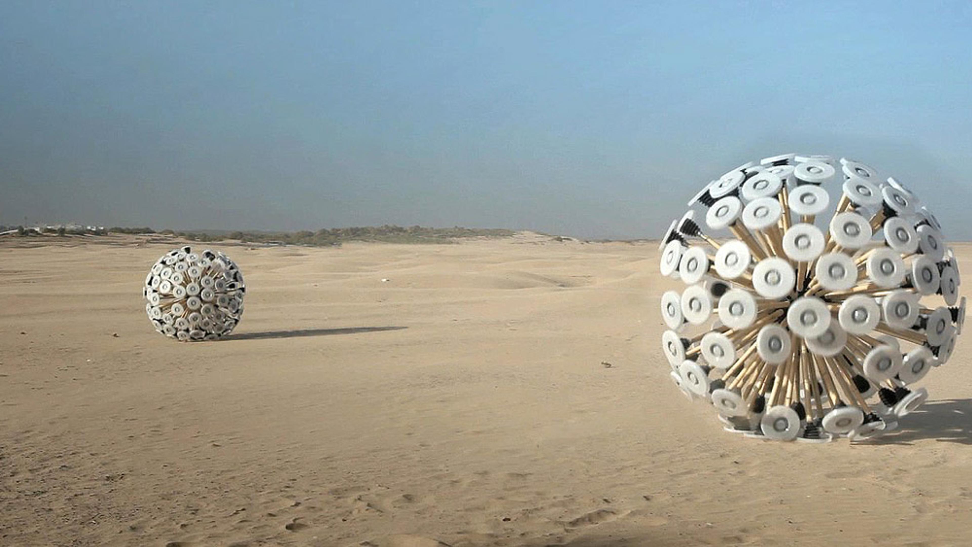 Two spherical, mechanical devices with rotating parts on a desert landscape under a clear sky.