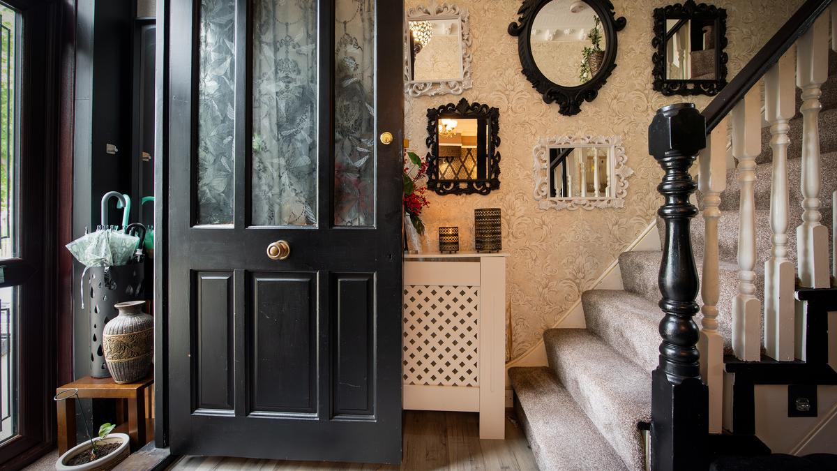A home entrance with a black front door, mirrored wall, umbrella stand and carpeted stairs.