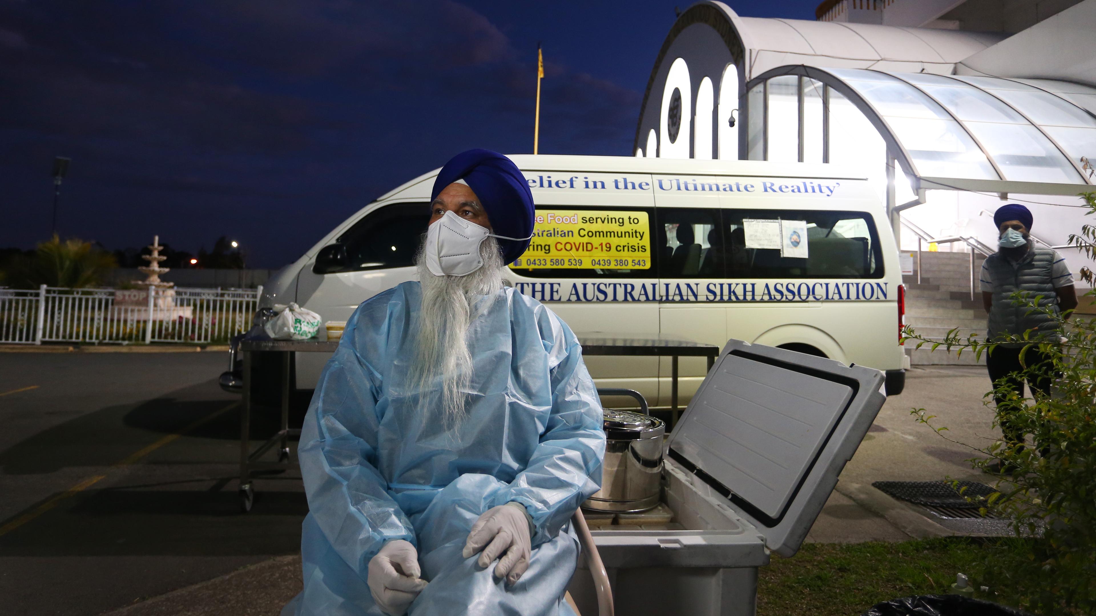 Photo of a man in protective gear and mask outdoors at night with a van labelled ‘The Australian Sikh Association’ in background.
