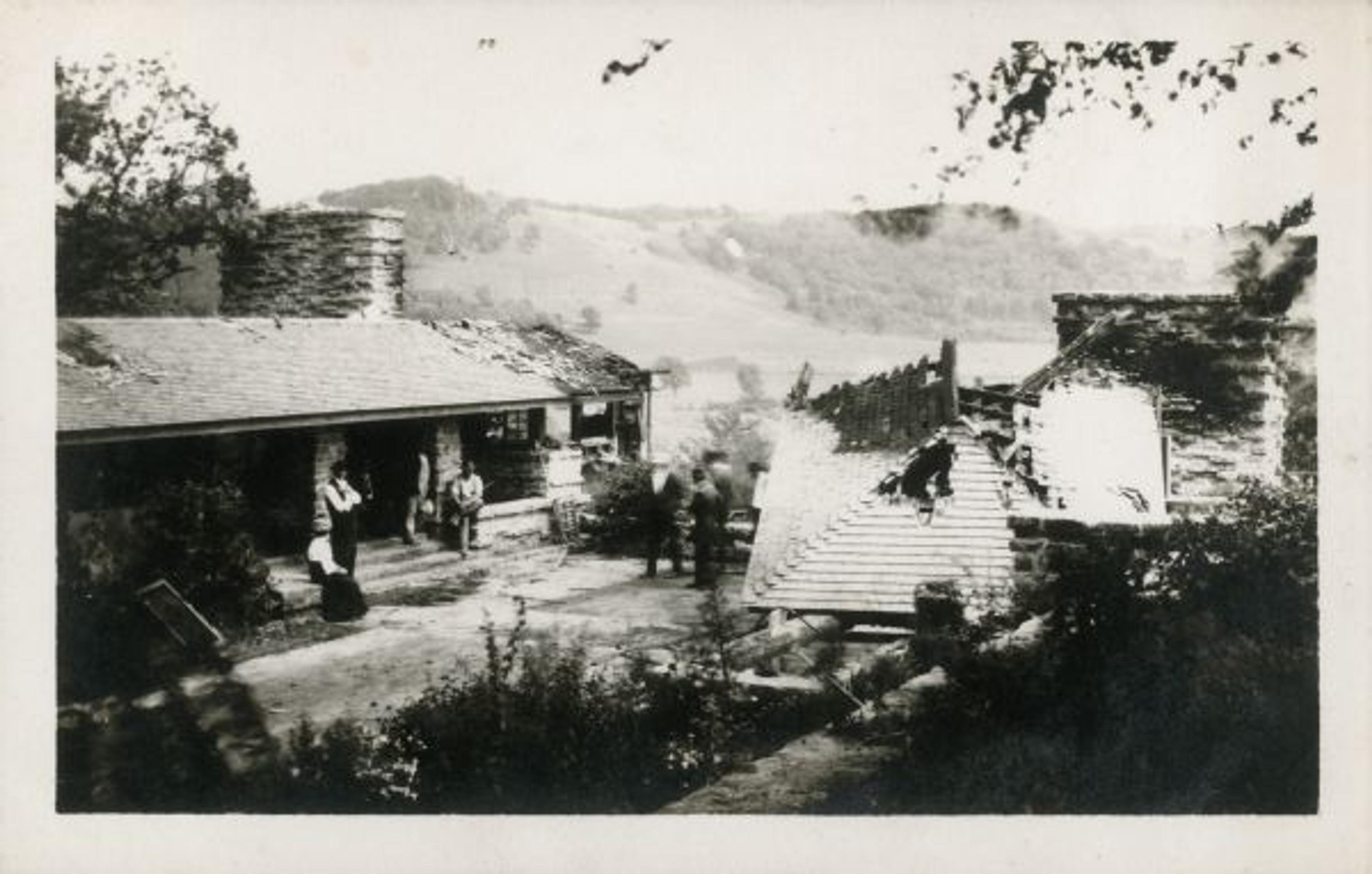 Black and white photo of people in the courtyard of a partially destroyed home, with a toppled and burnt roof.