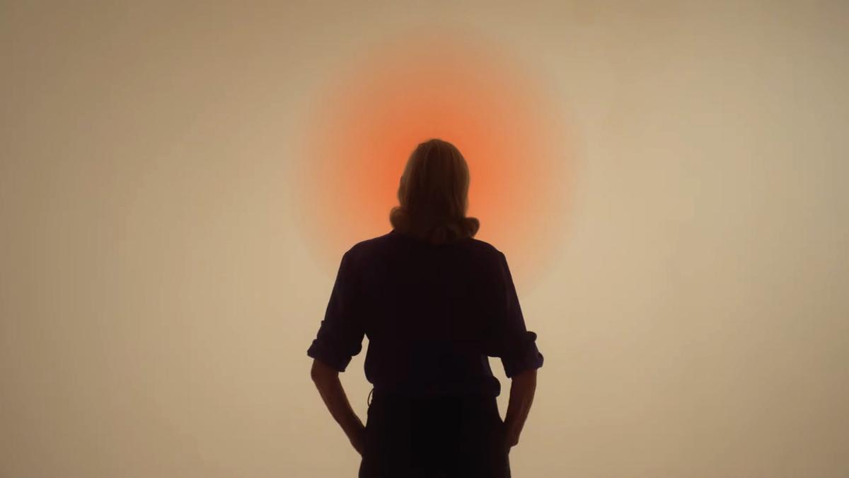 Silhouette of person standing before an orange light, creating a glowing halo effect on a neutral background.