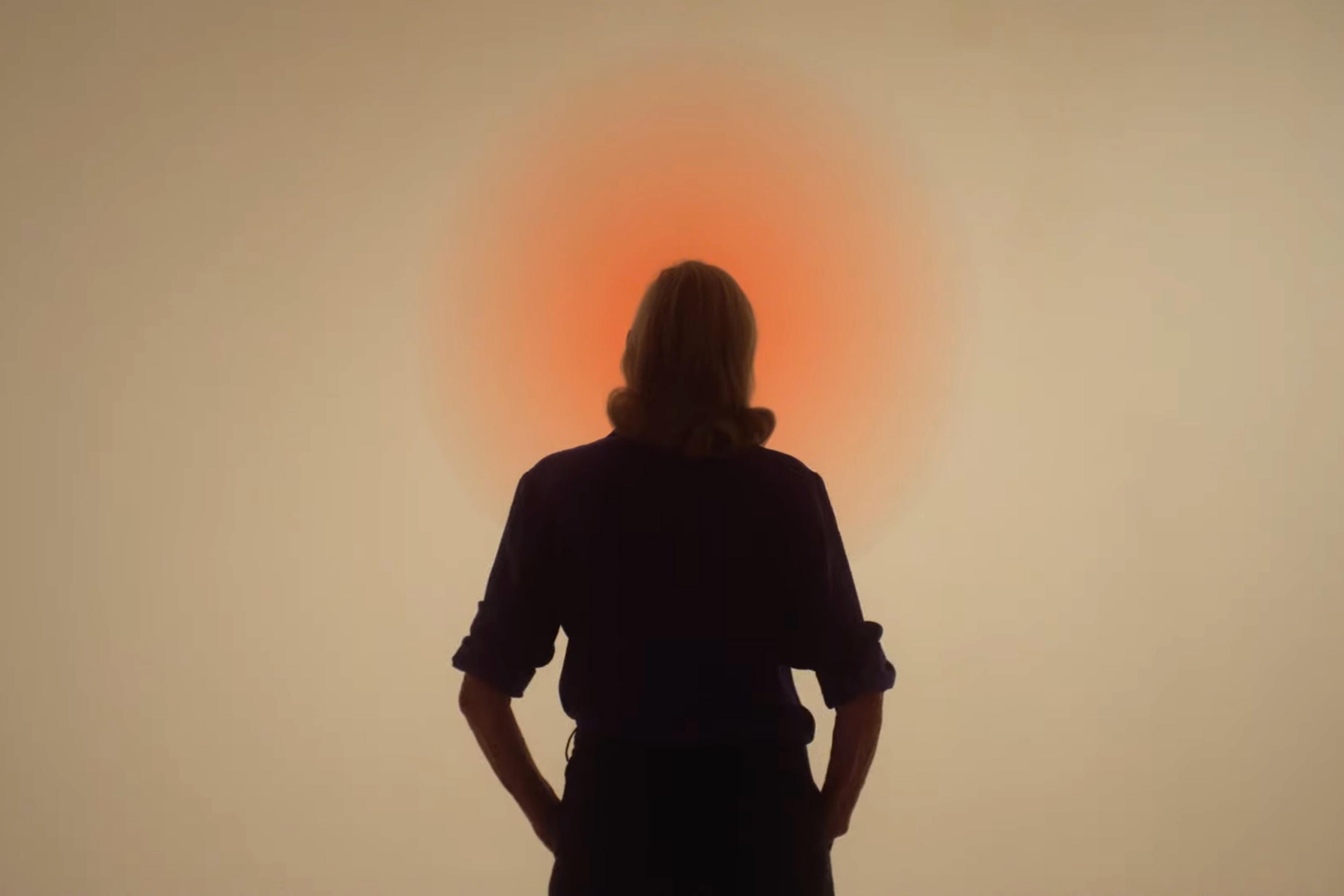Silhouette of person standing before an orange light, creating a glowing halo effect on a neutral background.