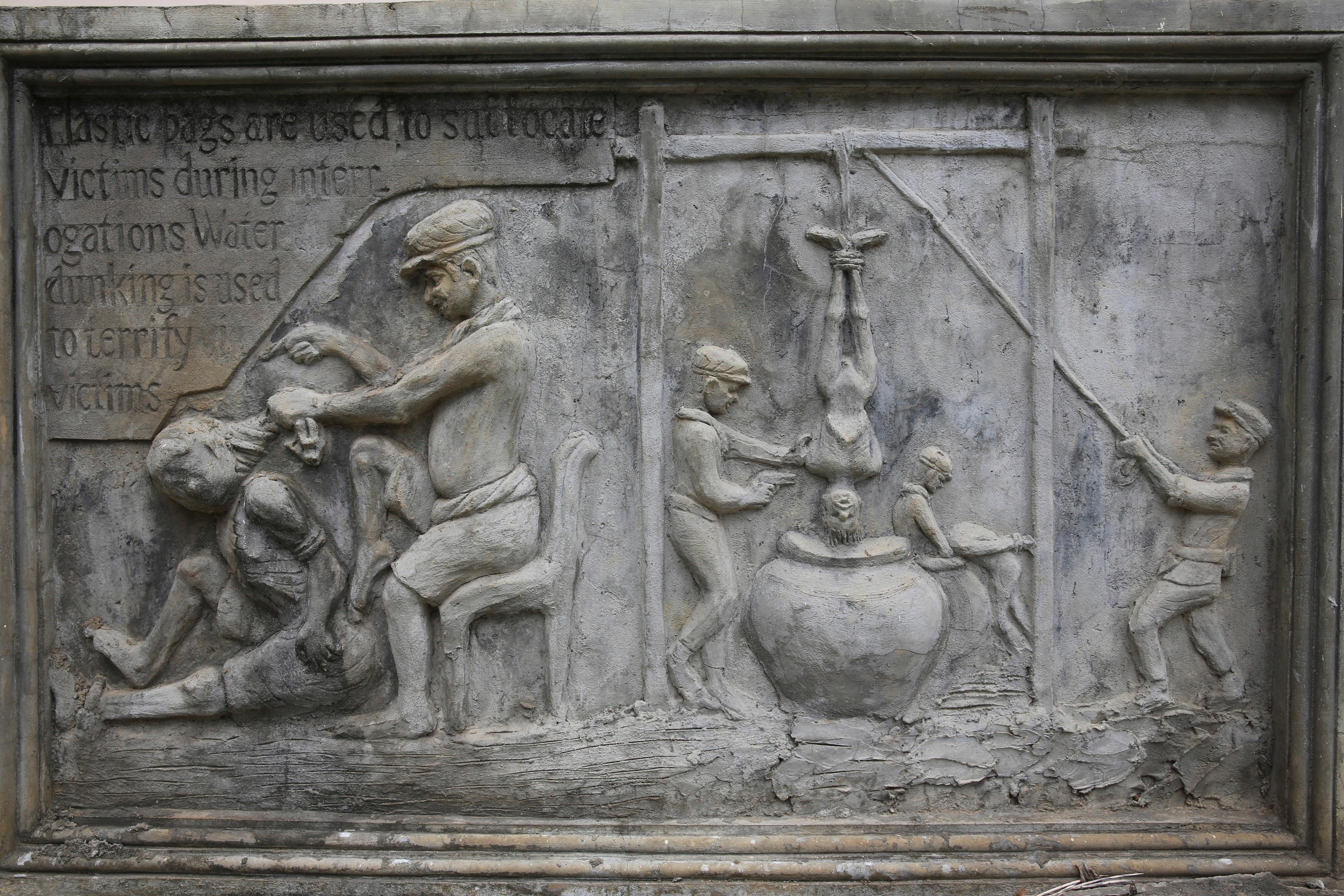 Stone relief depicting interrogation methods with figures enacting scenes of torture, accompanied by descriptive text.