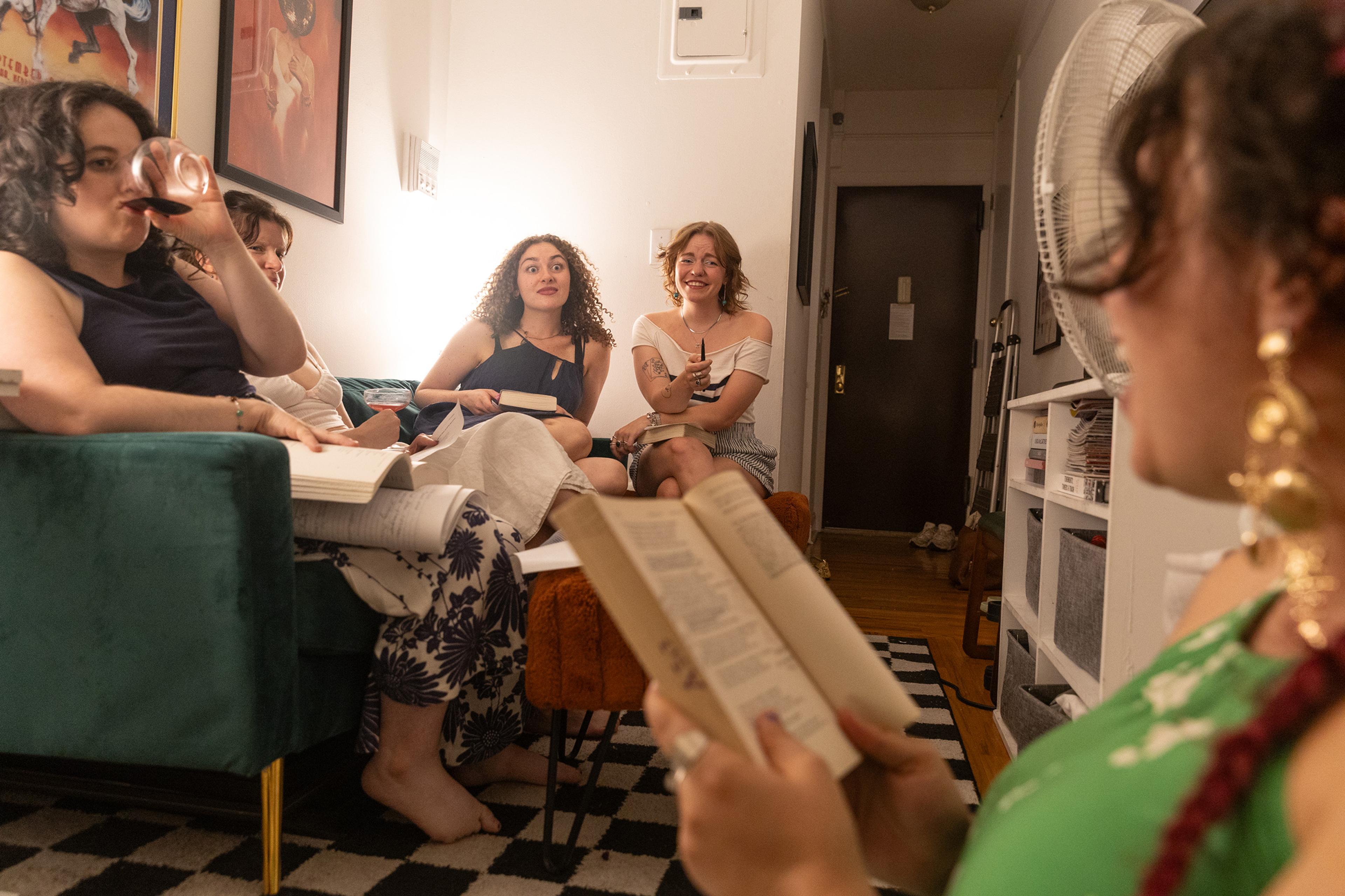 A book club meeting with five women, some reading, others chatting on a green sofa in a cosy living room.