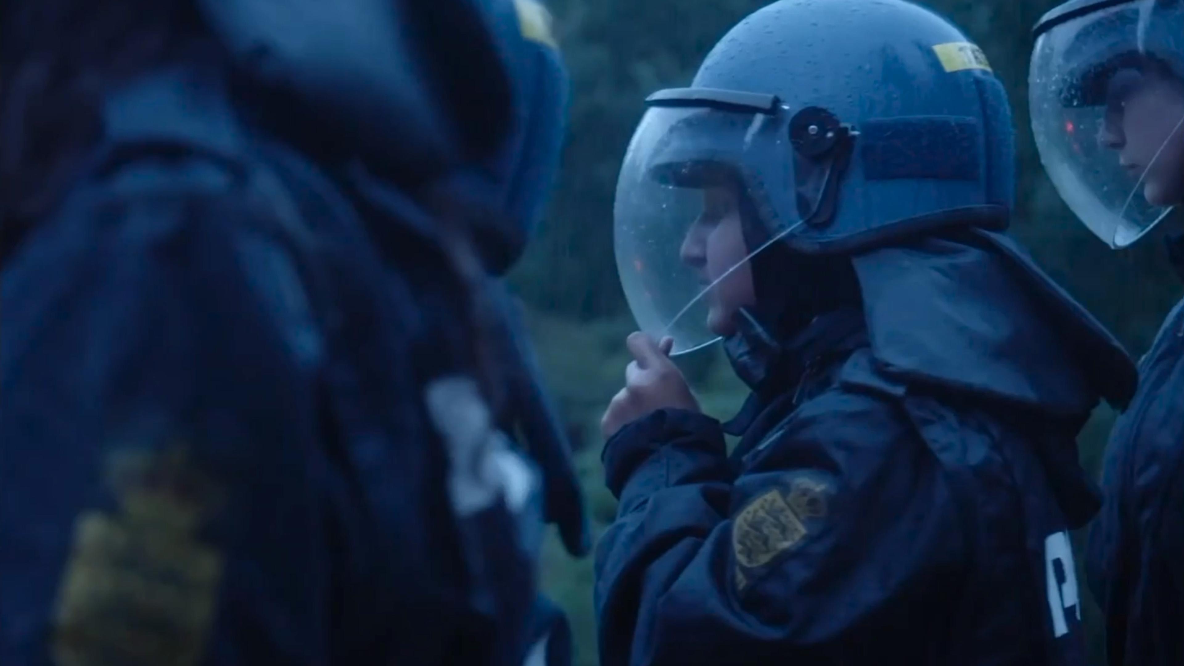 Young girls dressed in riot police helmets and gear standing outdoors in the rain.