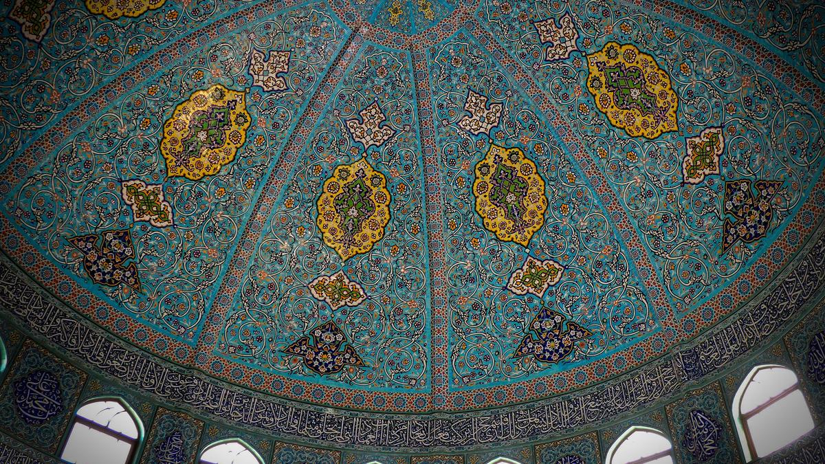 Intricate mosque dome with blue tiles and floral motifs photo. Arabic calligraphy surrounds the base with arched windows.