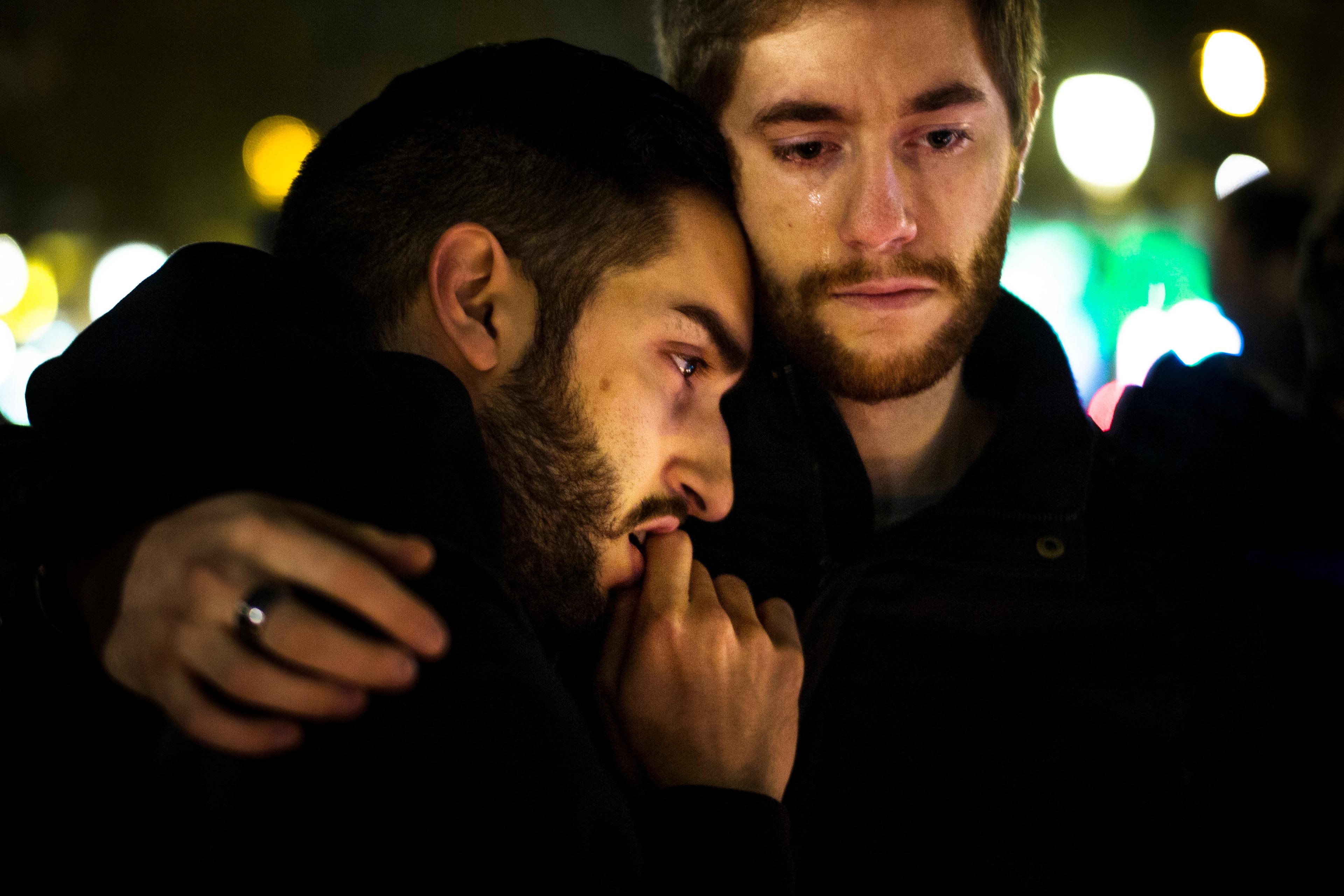 Photo of two men hugging in a sombre moment at night one has a tear running down his face.
