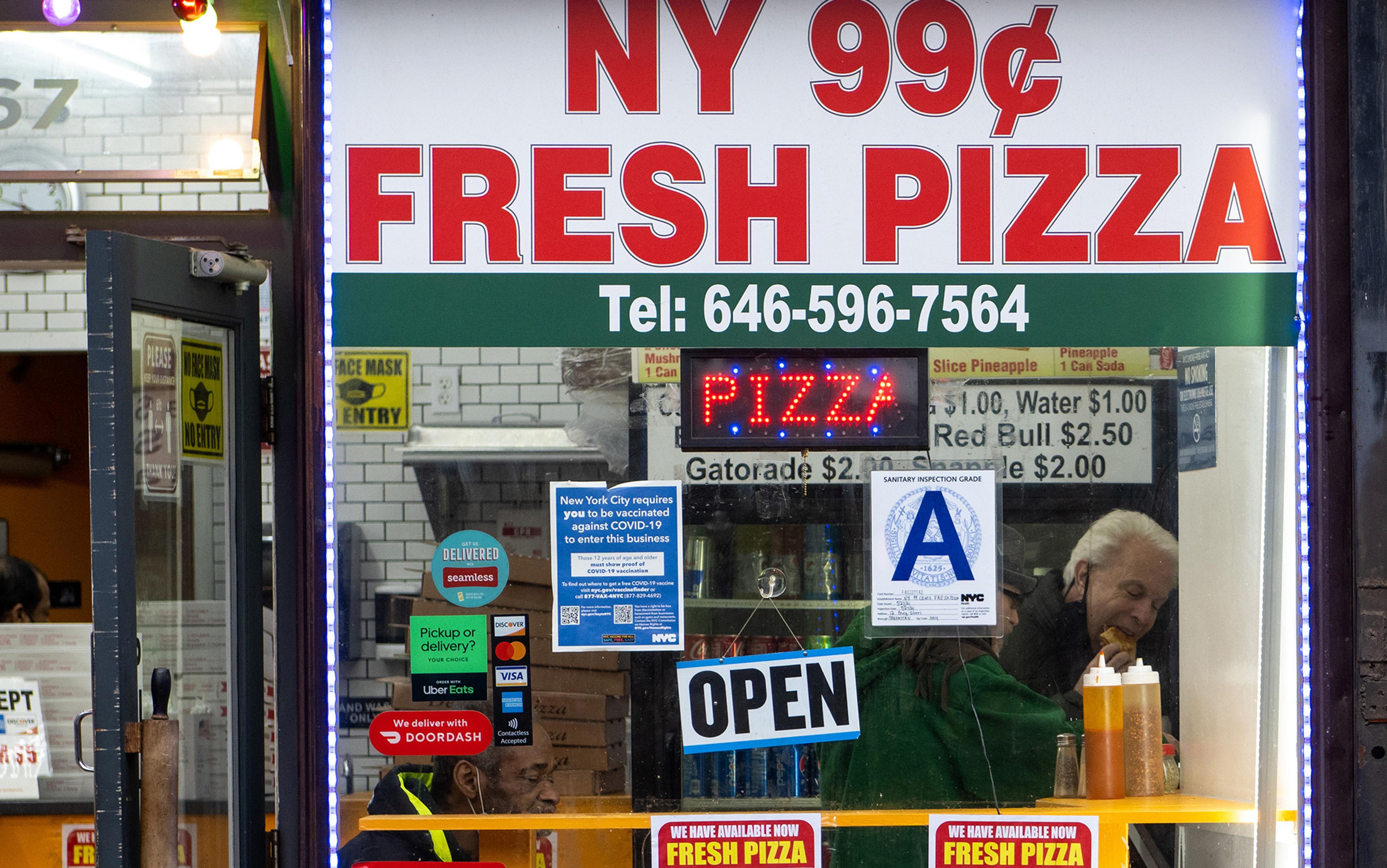 Shopfront of NY 99 Cent Fresh Pizza with an open sign, vaccine notice, and menu visible through the window.