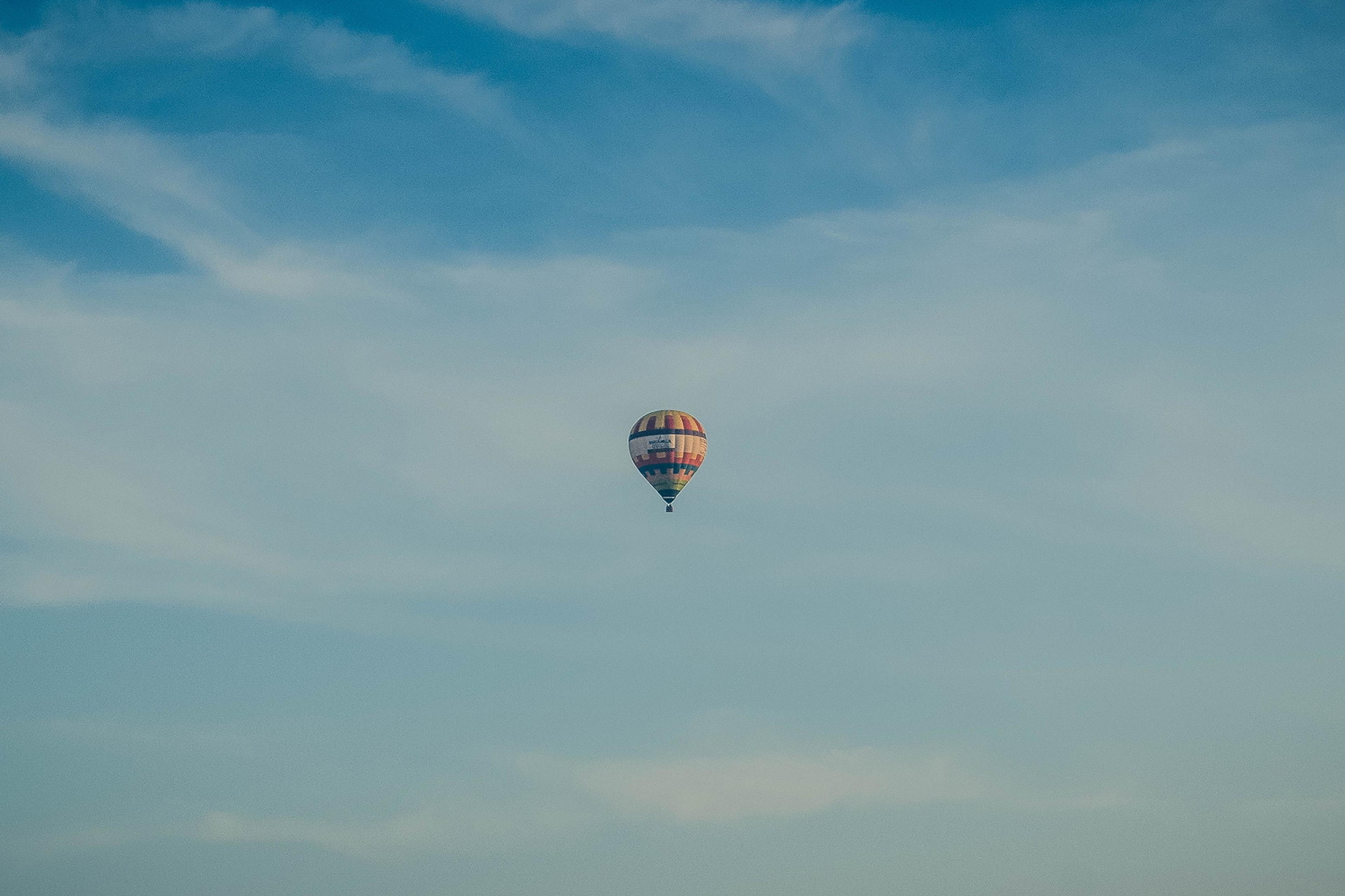 Photo of a single hot air balloon in a clear blue sky with light clouds.