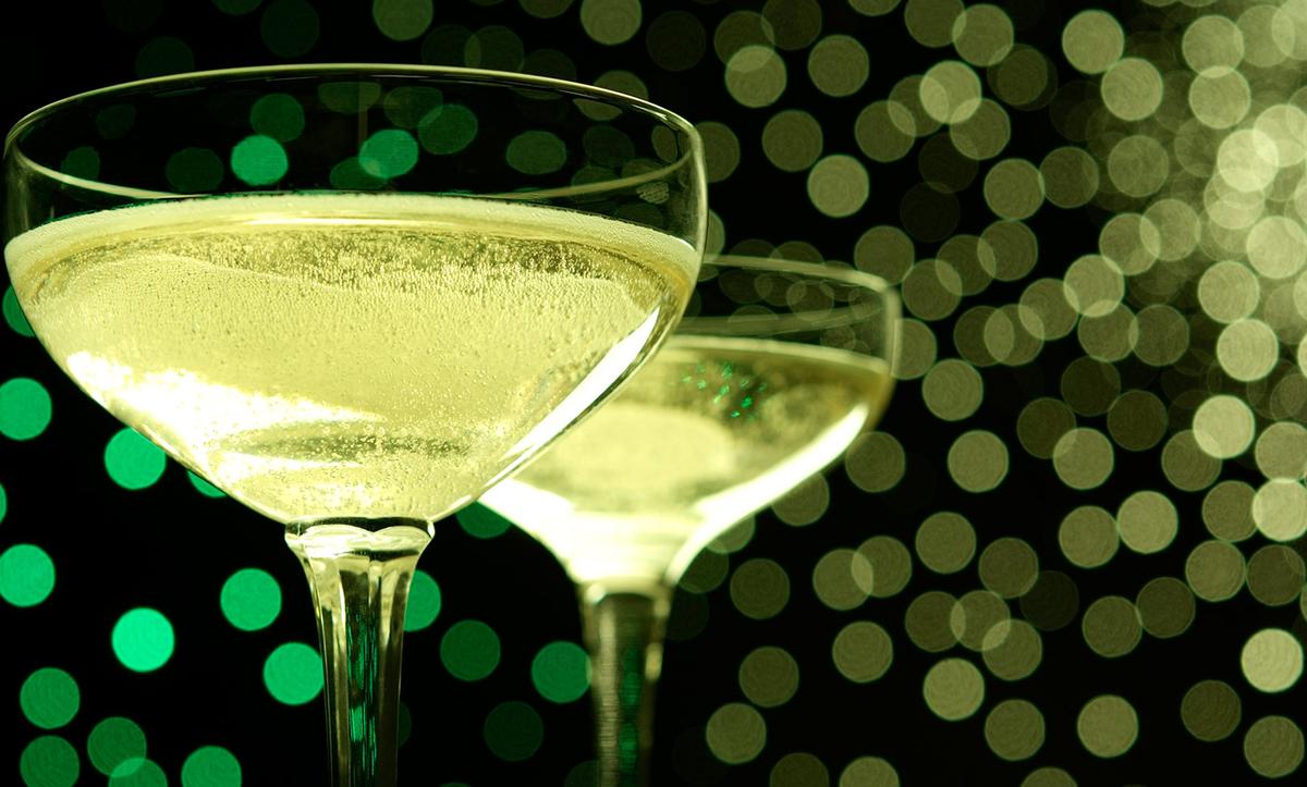 Two champagne glasses filled with bubbly liquid against a background of green and gold bokeh lights.