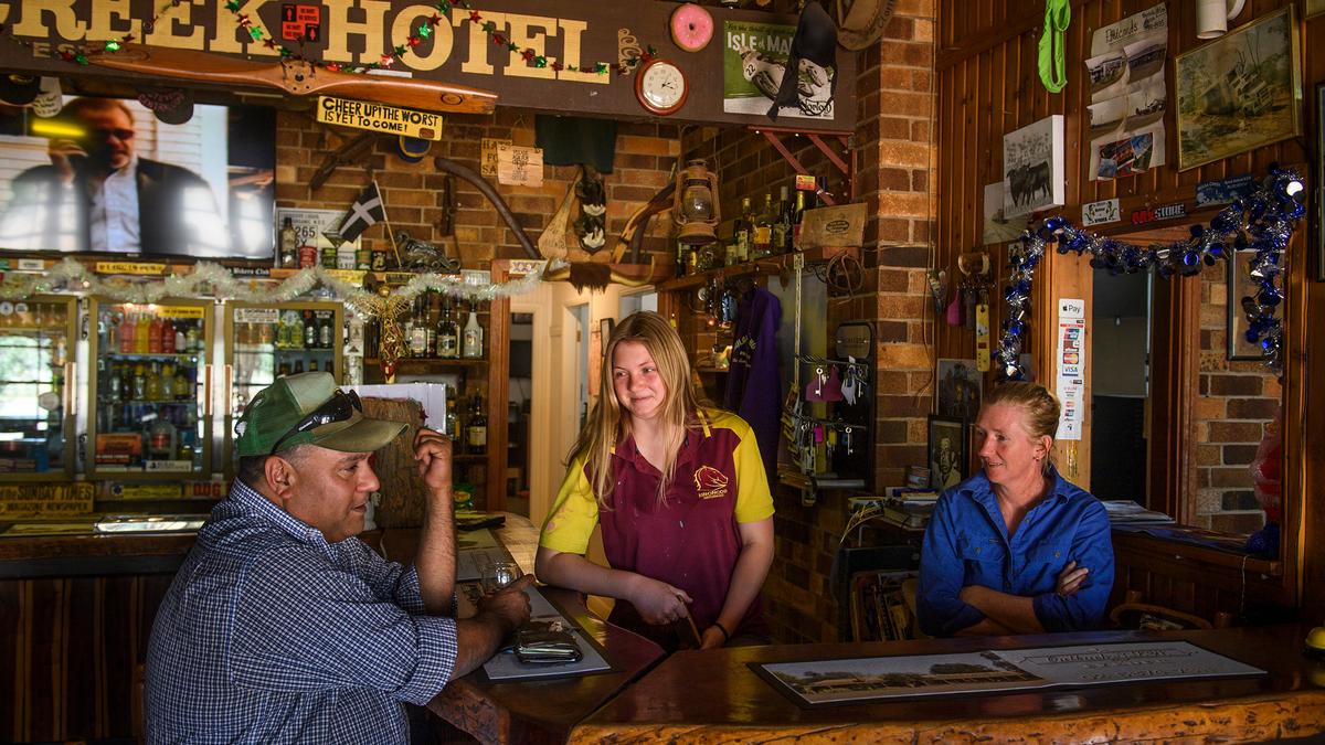 Three people chatting at a rustic bar in a pub, with a brick interior and various decorations.