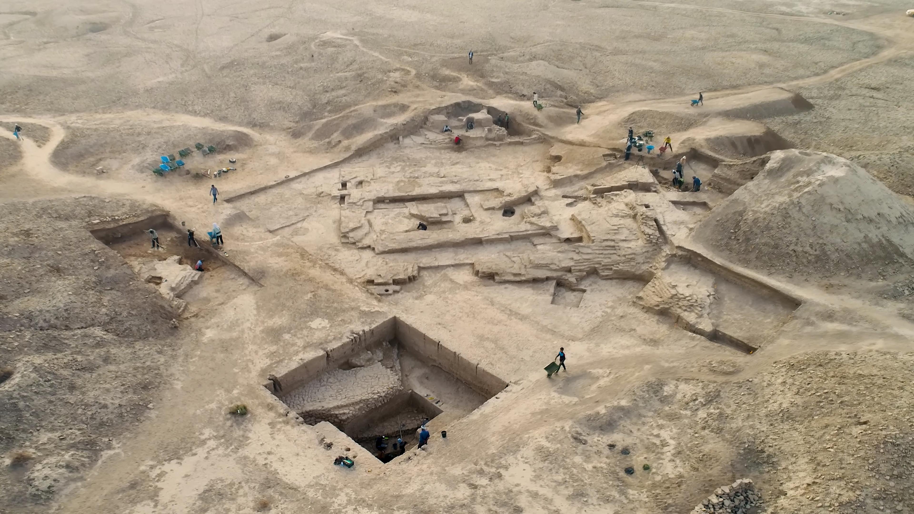 Aerial photo of an archaeological excavation site in a barren landscape with workers digging and examining the area.