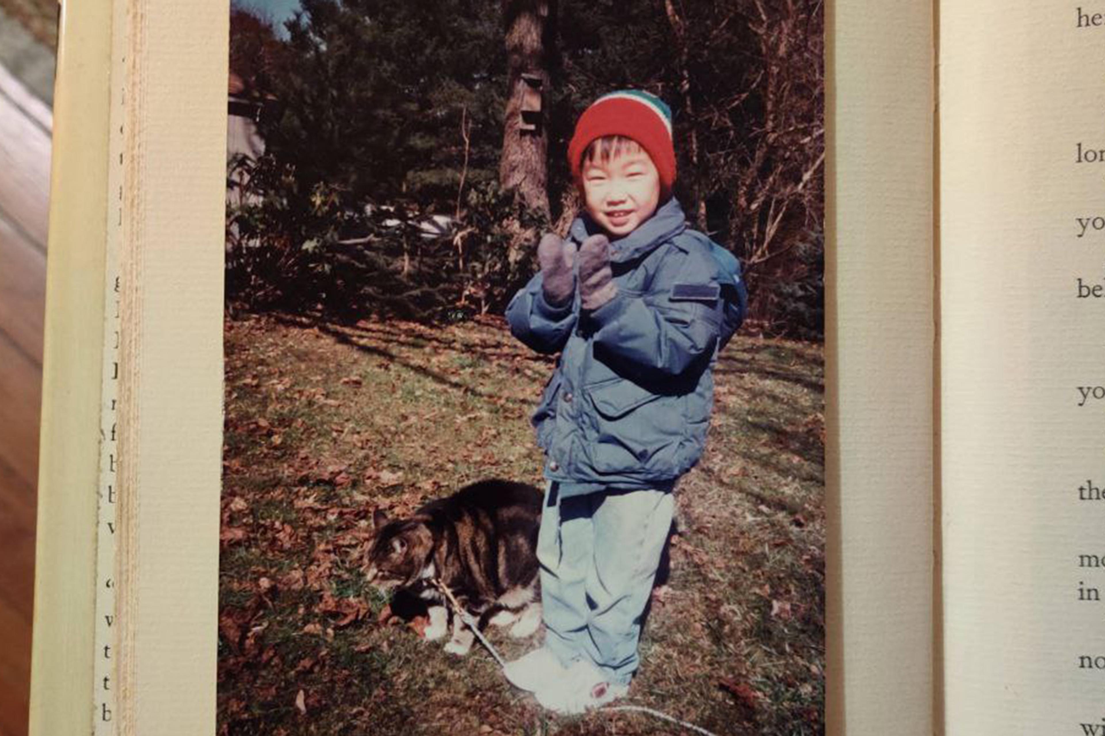 Photo of a child in winter clothing standing next to a cat outdoors on a sunny day, with text from a book visible.
