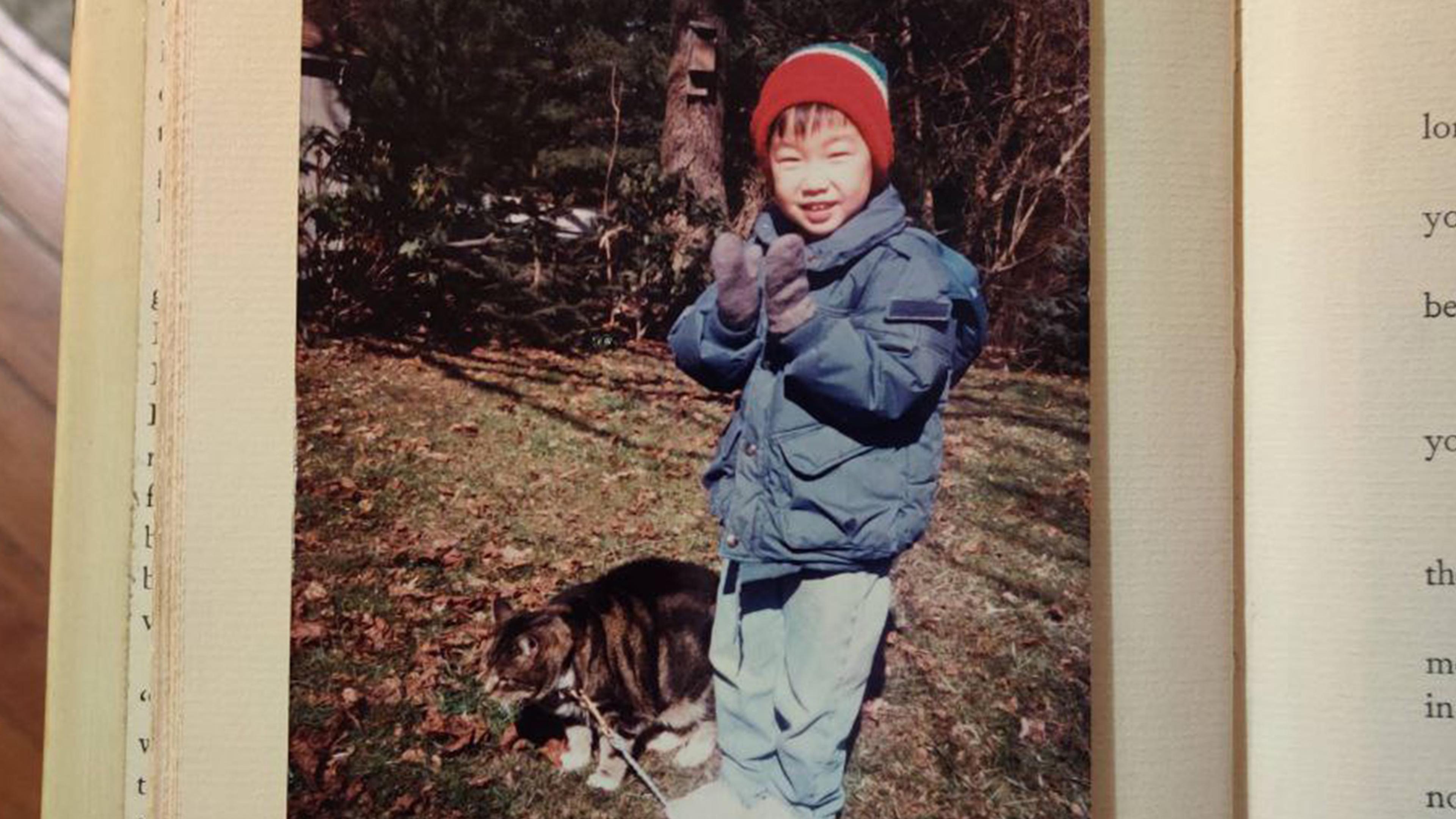 Photo of a child in winter clothing standing next to a cat outdoors on a sunny day, with text from a book visible.