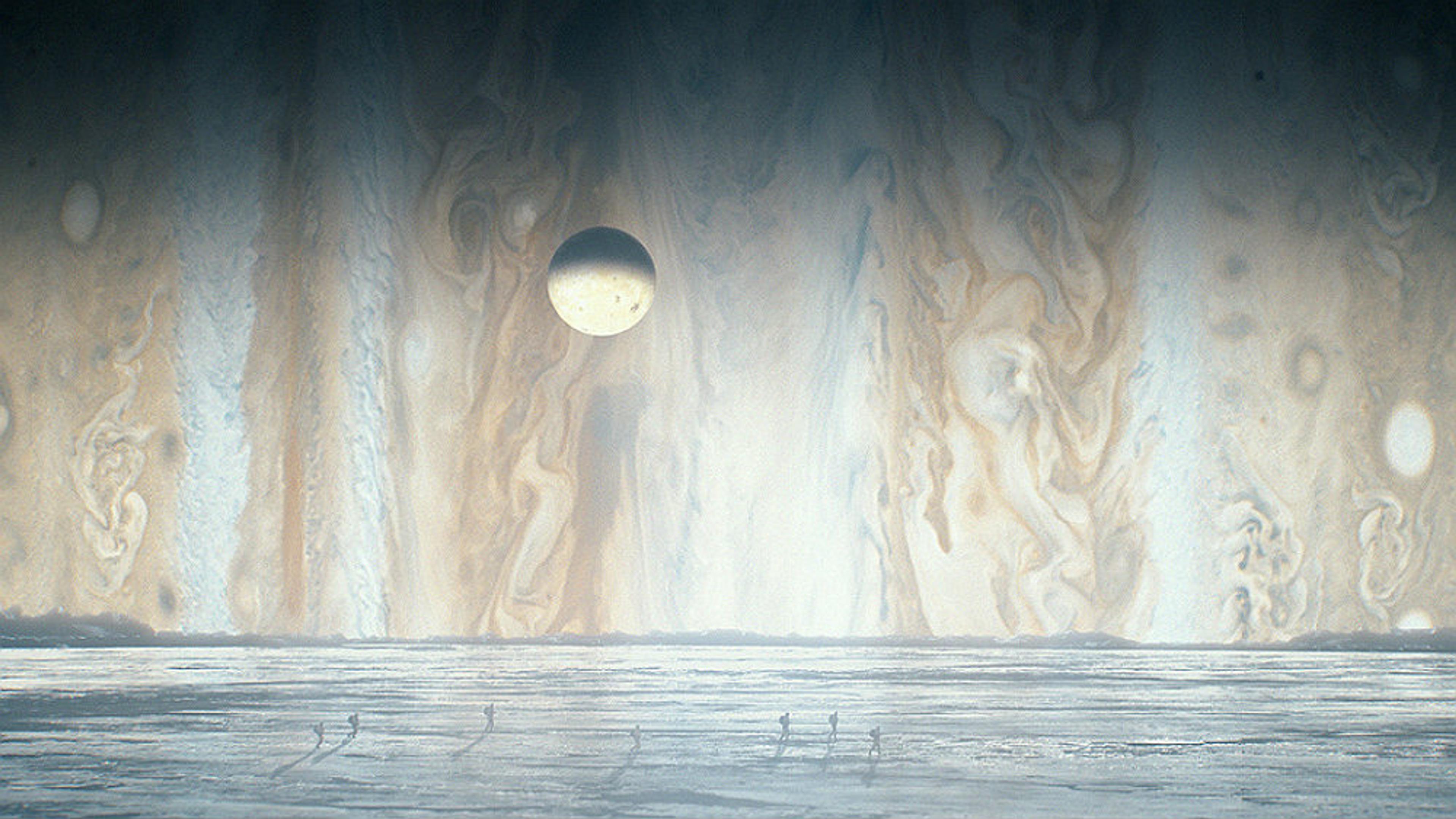 Digital artwork of an icy landscape with Jupiter and a moon in the background; small figures walk on the ice in the foreground.