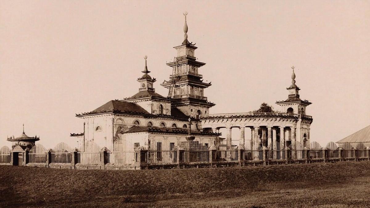 Sepia-toned photo of an ornate building with spires surrounded by a fence, set on a grassy area under a clear sky.