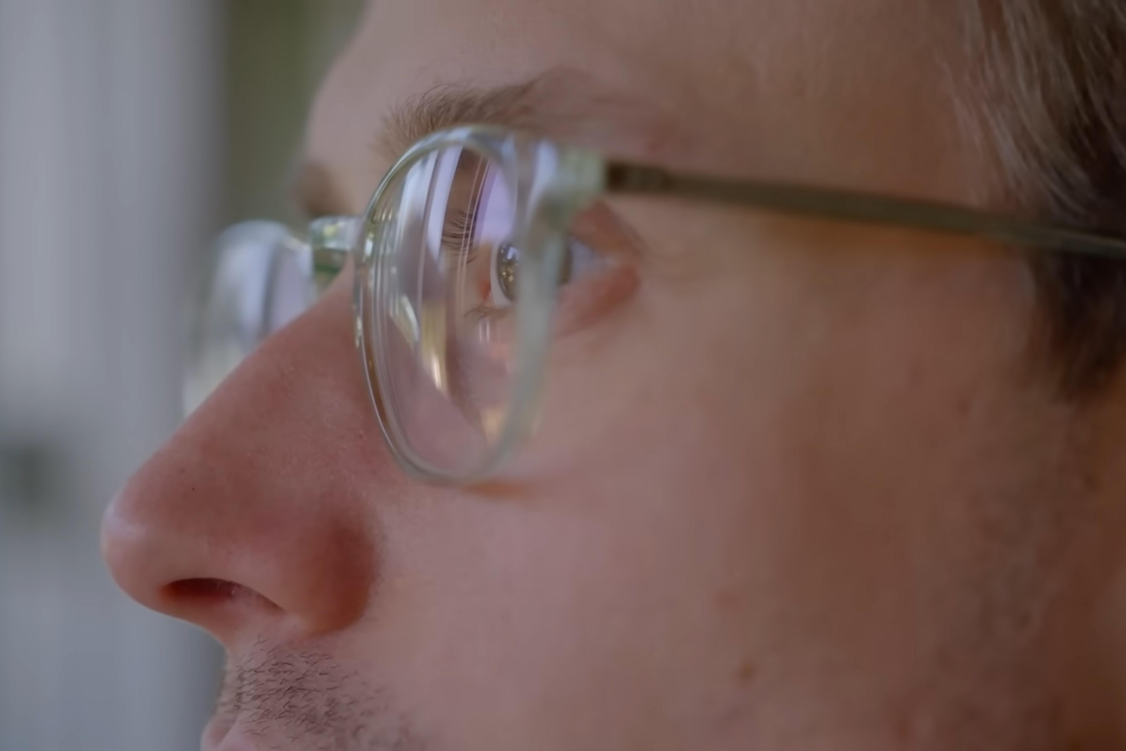 Close-up photo of a person’s face in profile wearing glasses looking out of a window, with reflections in the lenses.