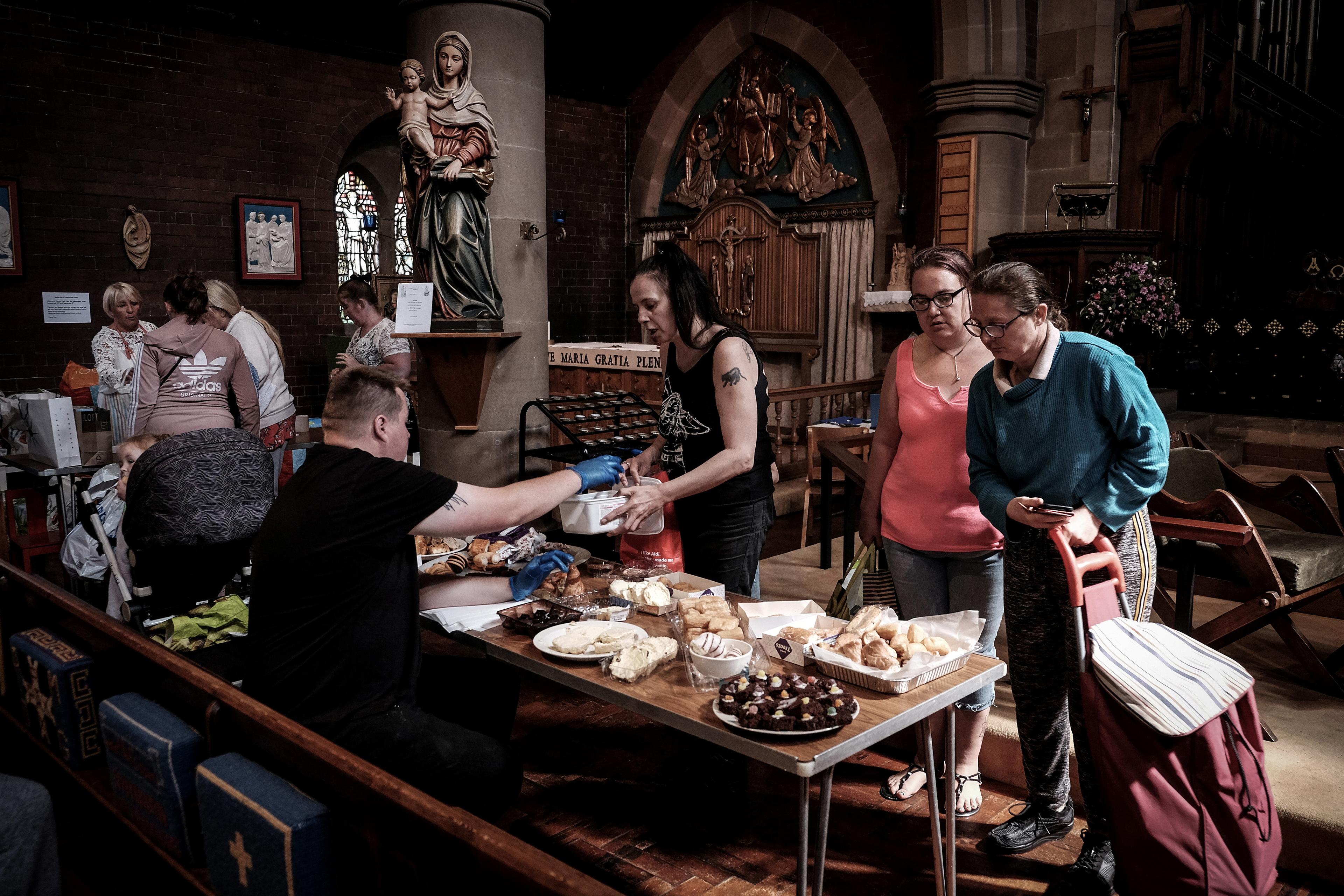 Photo of people gathering around a table with food inside a church. A statue of Mary and child is visible in the background.