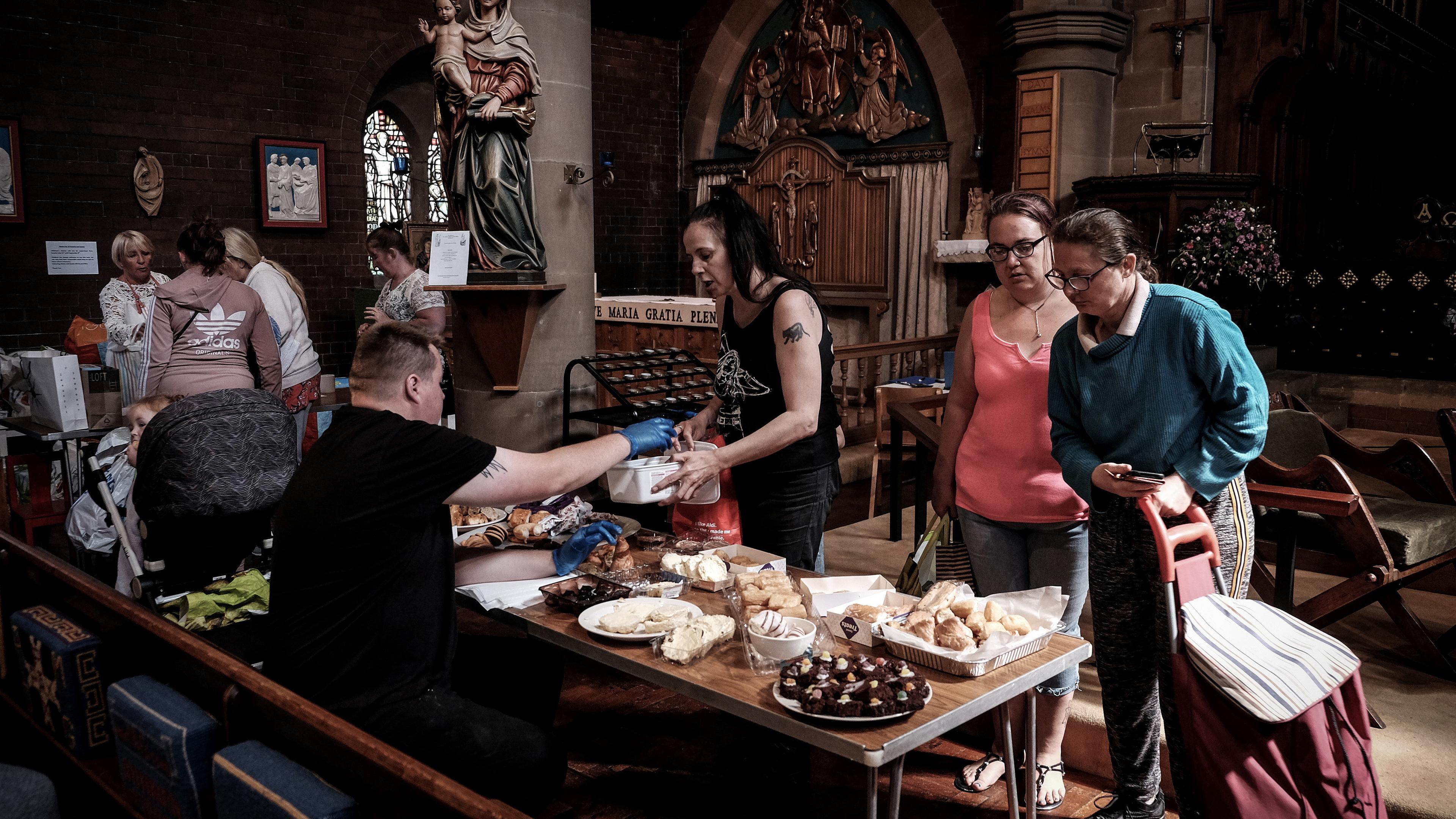 Photo of people gathering around a table with food inside a church. A statue of Mary and child is visible in the background.