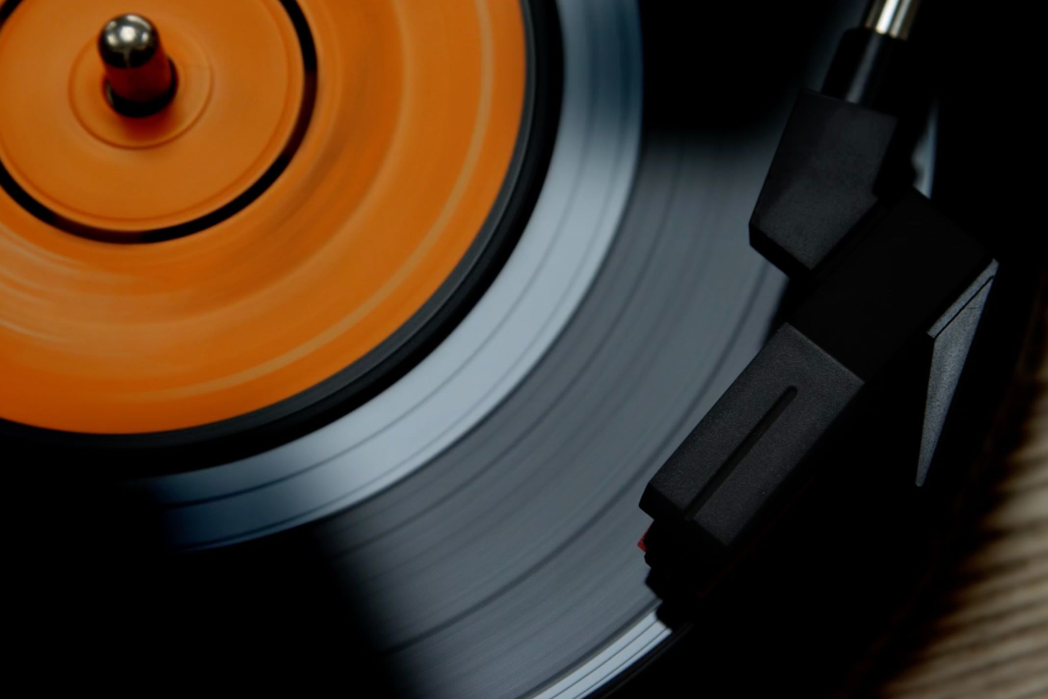 A spinning vinyl record with an orange label and a turntable needle in motion on the black grooved surface.