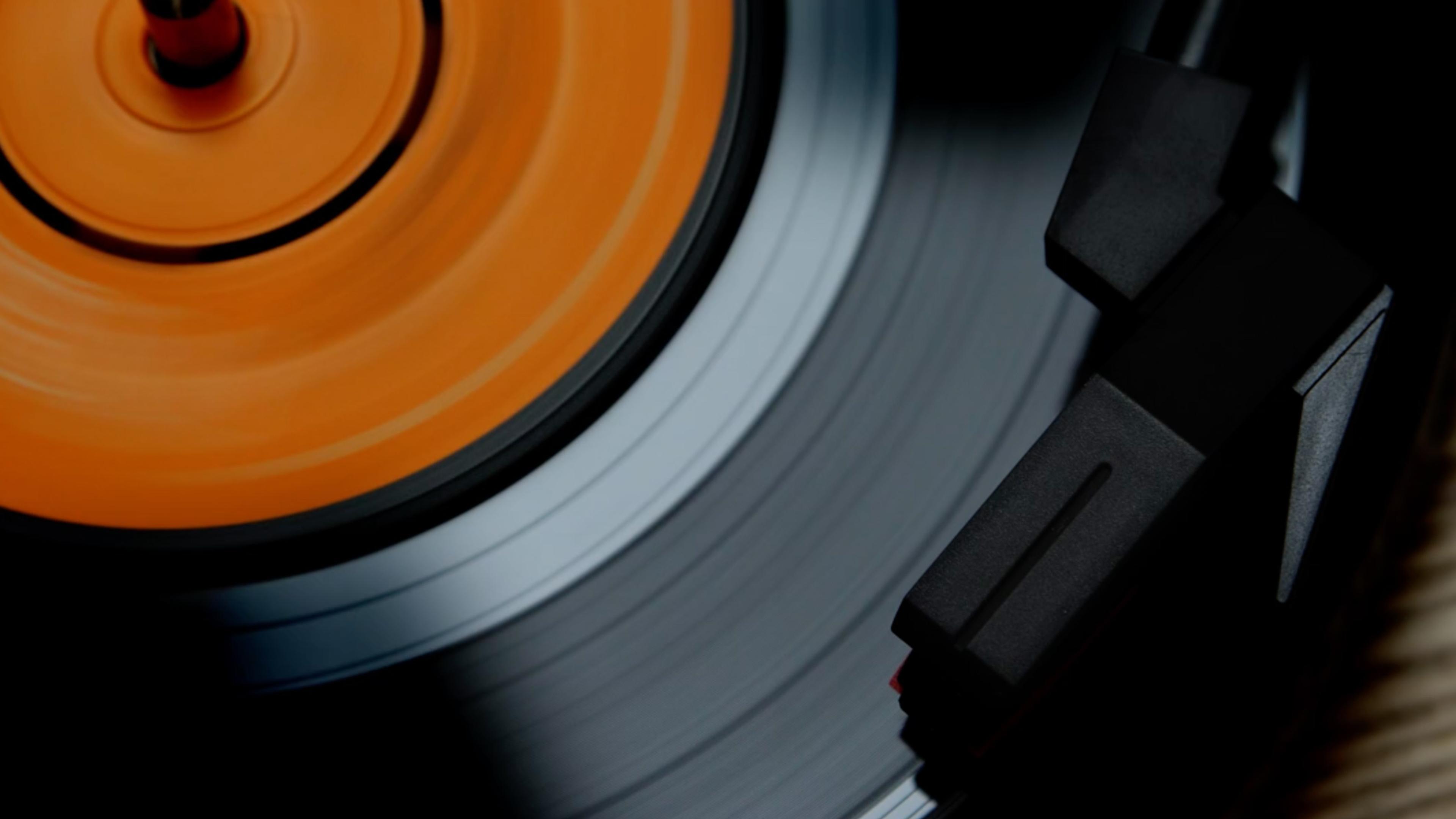 A spinning vinyl record with an orange label and a turntable needle in motion on the black grooved surface.