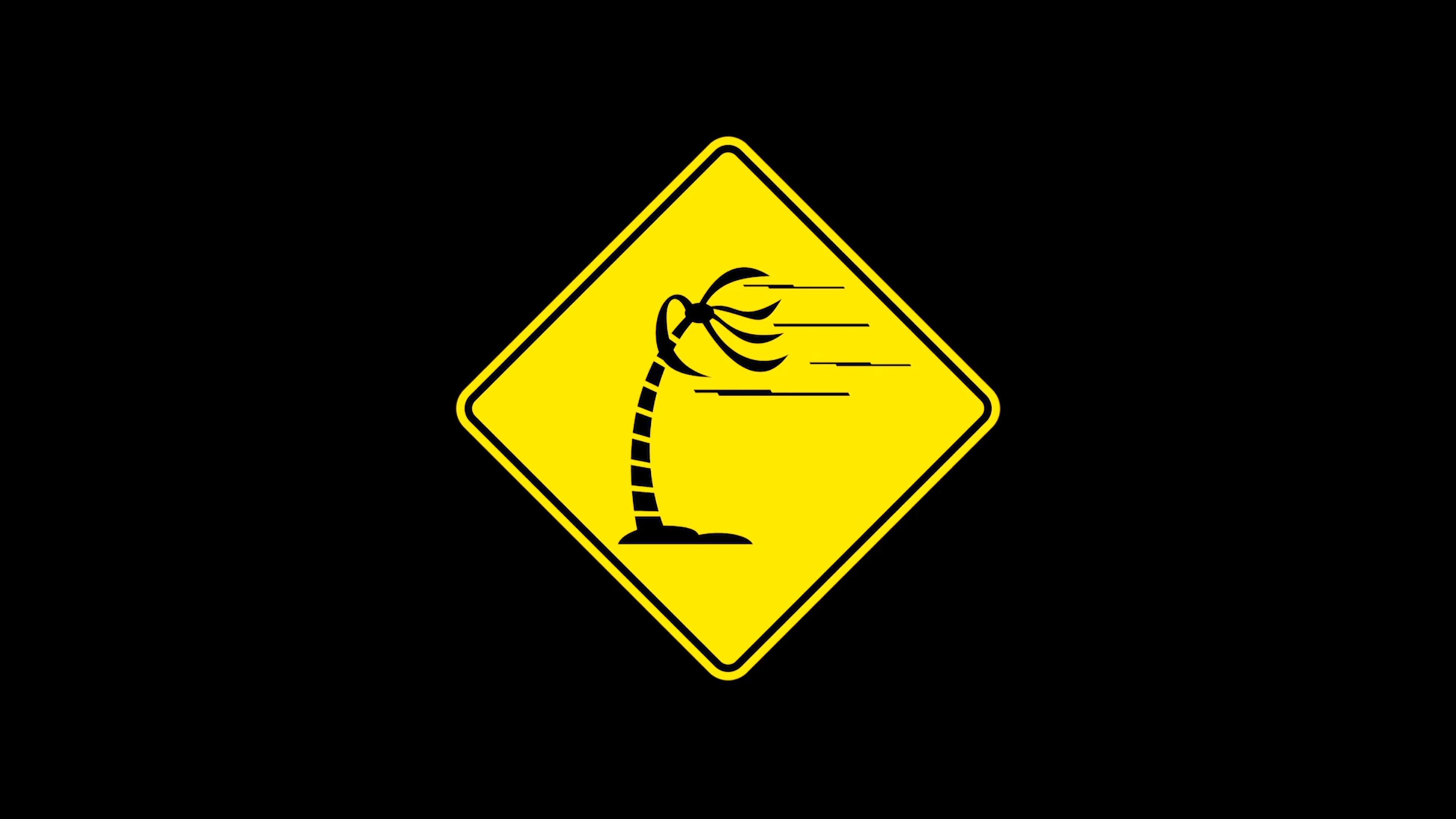 Yellow warning sign with a black palm tree bent over in strong wind, signifying severe weather or wind conditions.