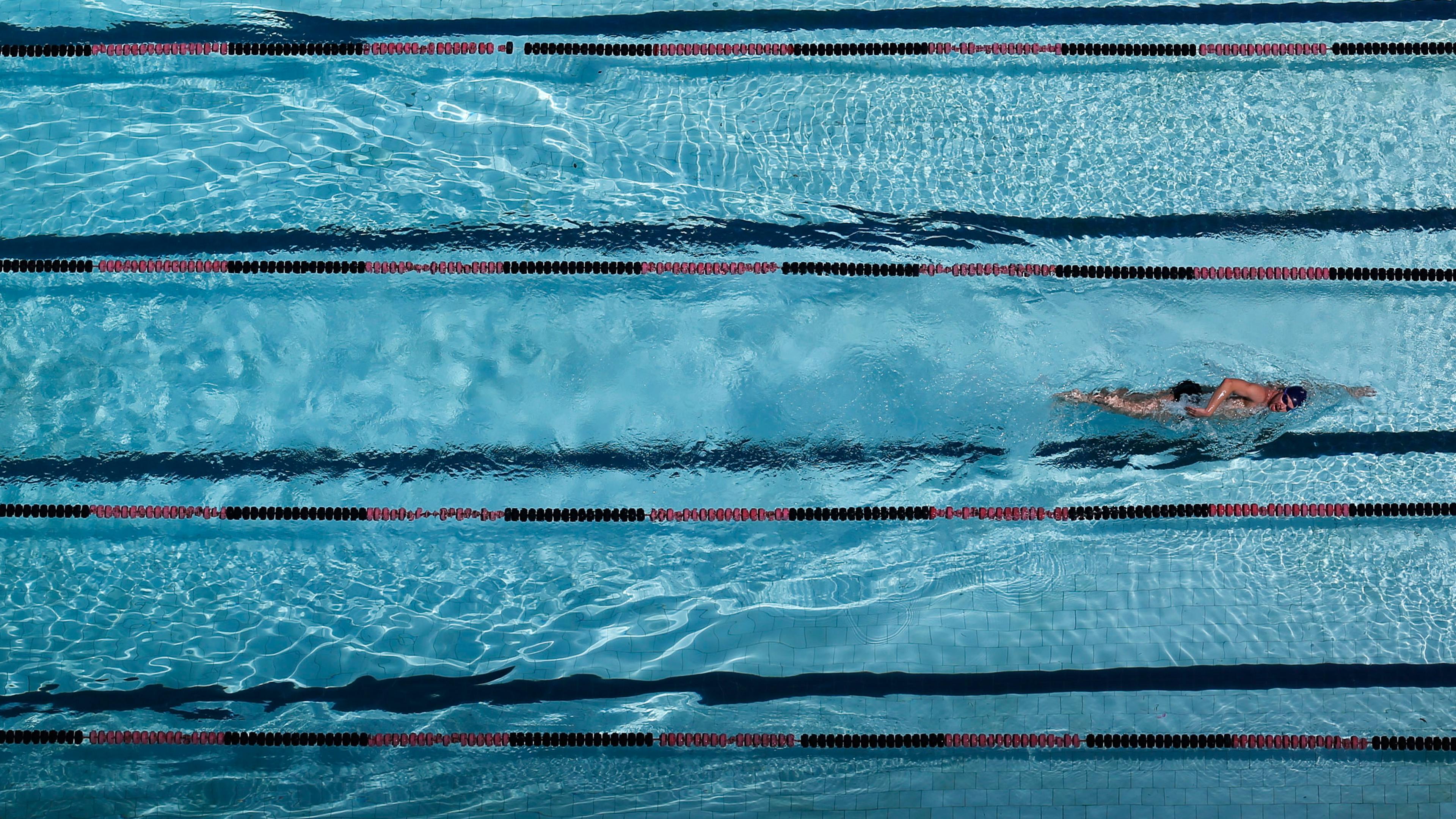 Photo of an overhead view of a swimmer in a lane of a clear blue swimming pool with lane dividers.