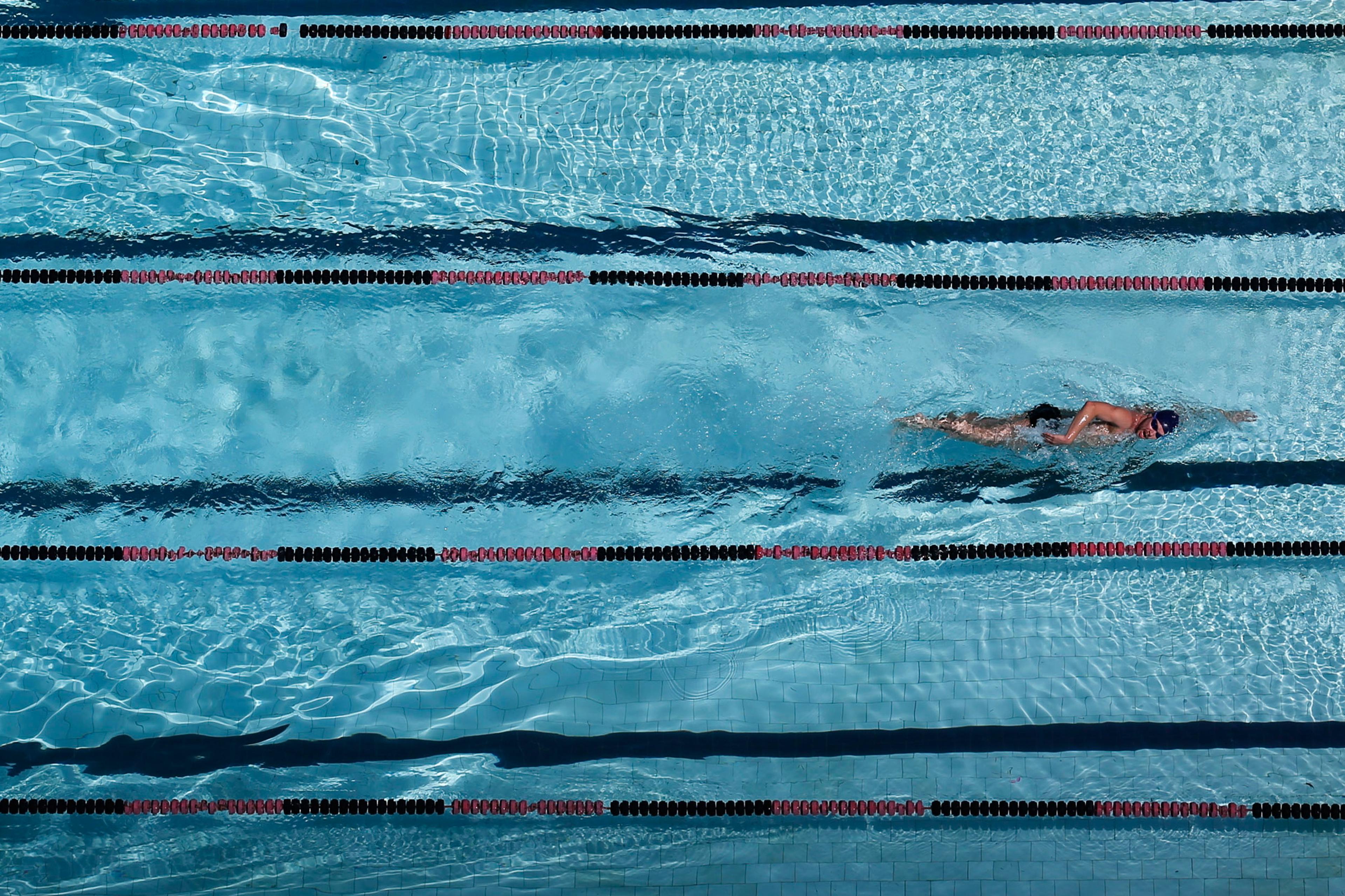 Photo of an overhead view of a swimmer in a lane of a clear blue swimming pool with lane dividers.