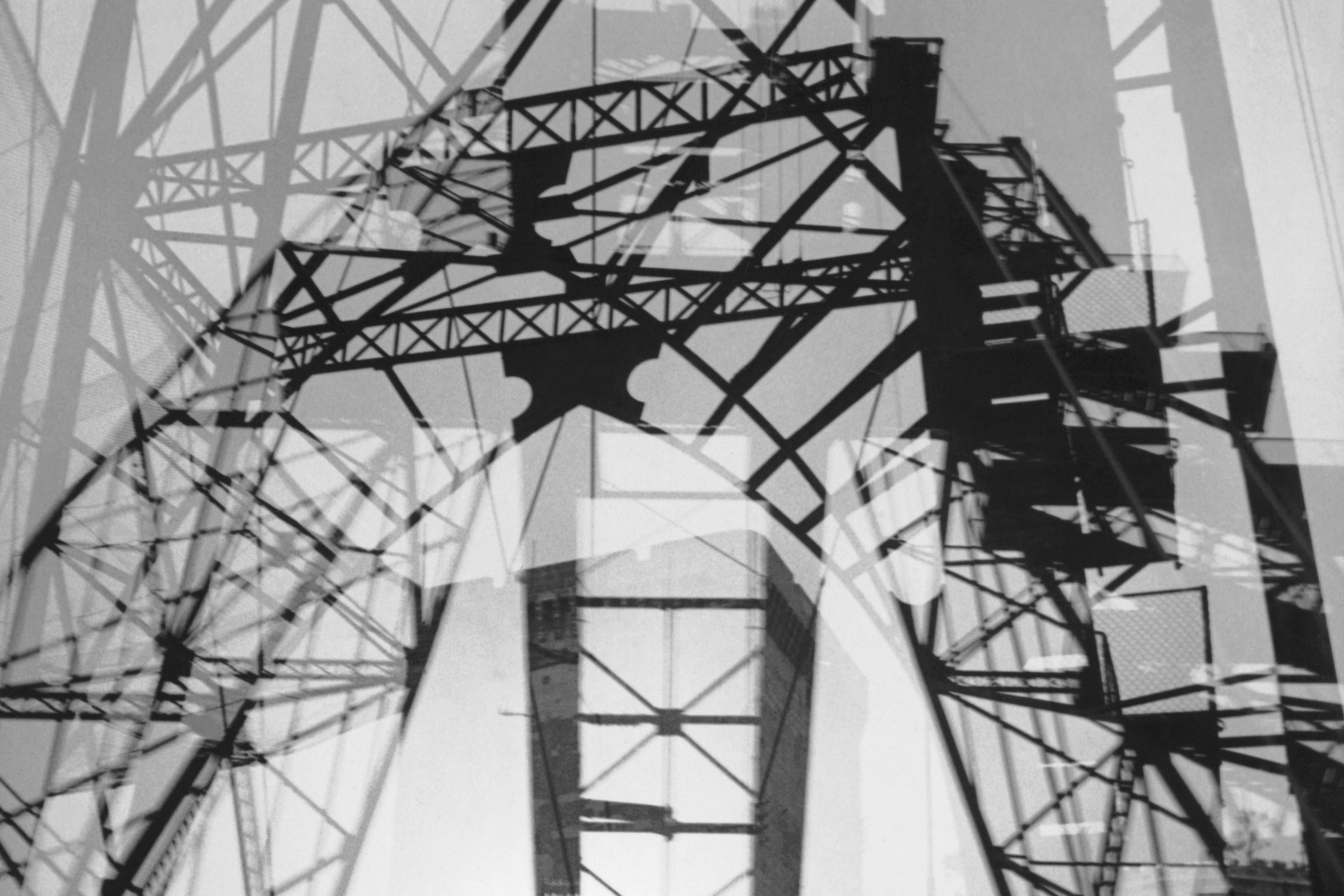 Black and white photo of overlapping industrial structures with geometric patterns and shadows creating a complex design.