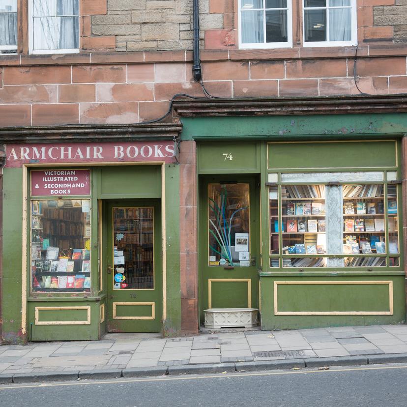 Photo of a street with a person entering a doorway to the left and a bookshop named Armchair Books displaying books in its windows.