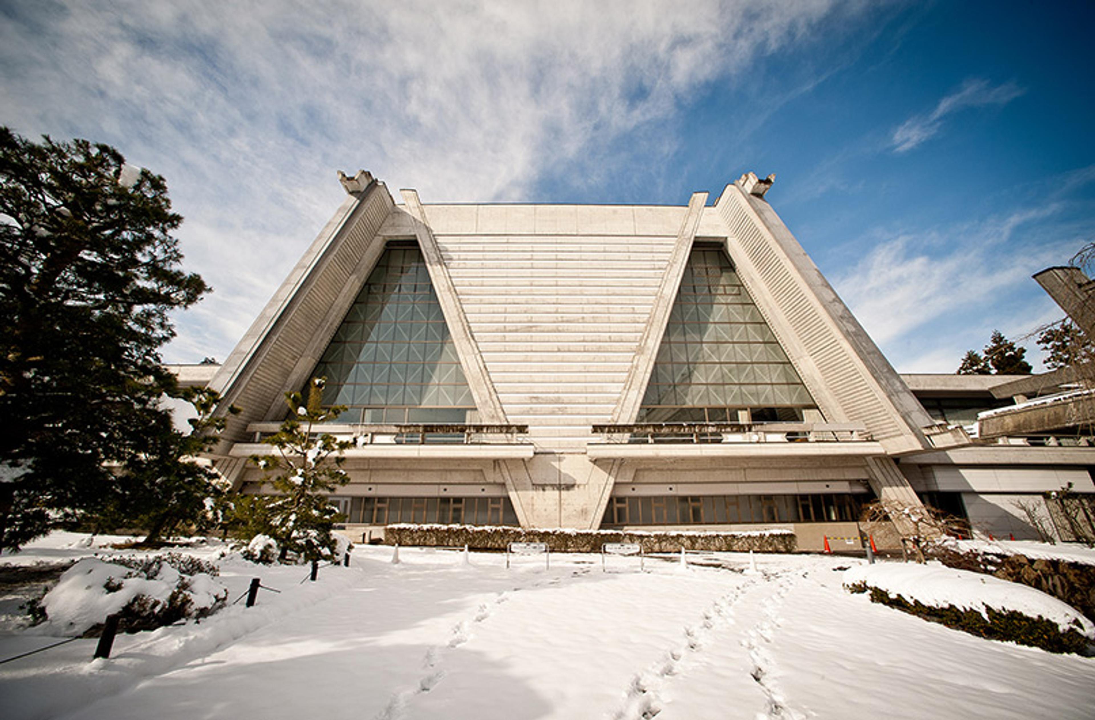 A modern concrete building with triangular structures in a snowy landscape, clear sky and footprints leading to the entrance.