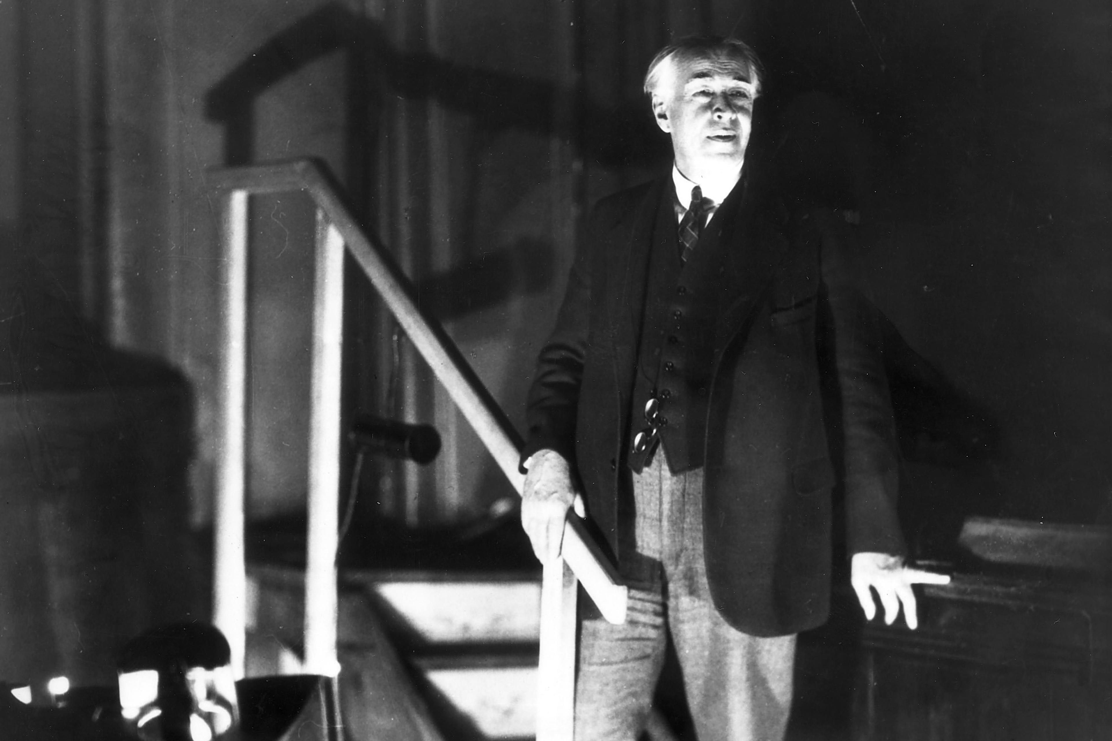 Black and white photo of a man in a suit standing by stairs in dramatic lighting.