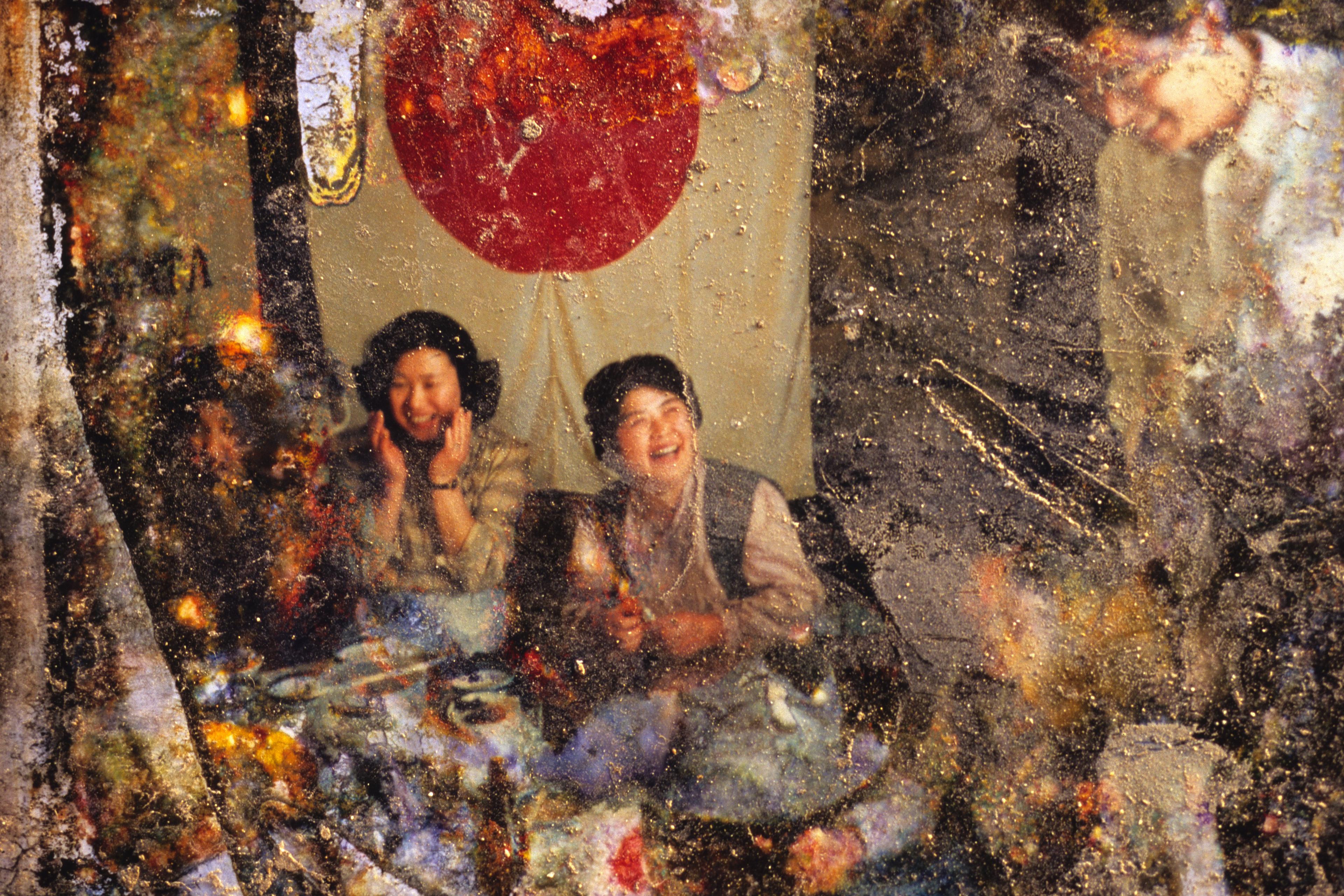 A damaged photo of people laughing at a table, with a large red circle on a banner in the background.