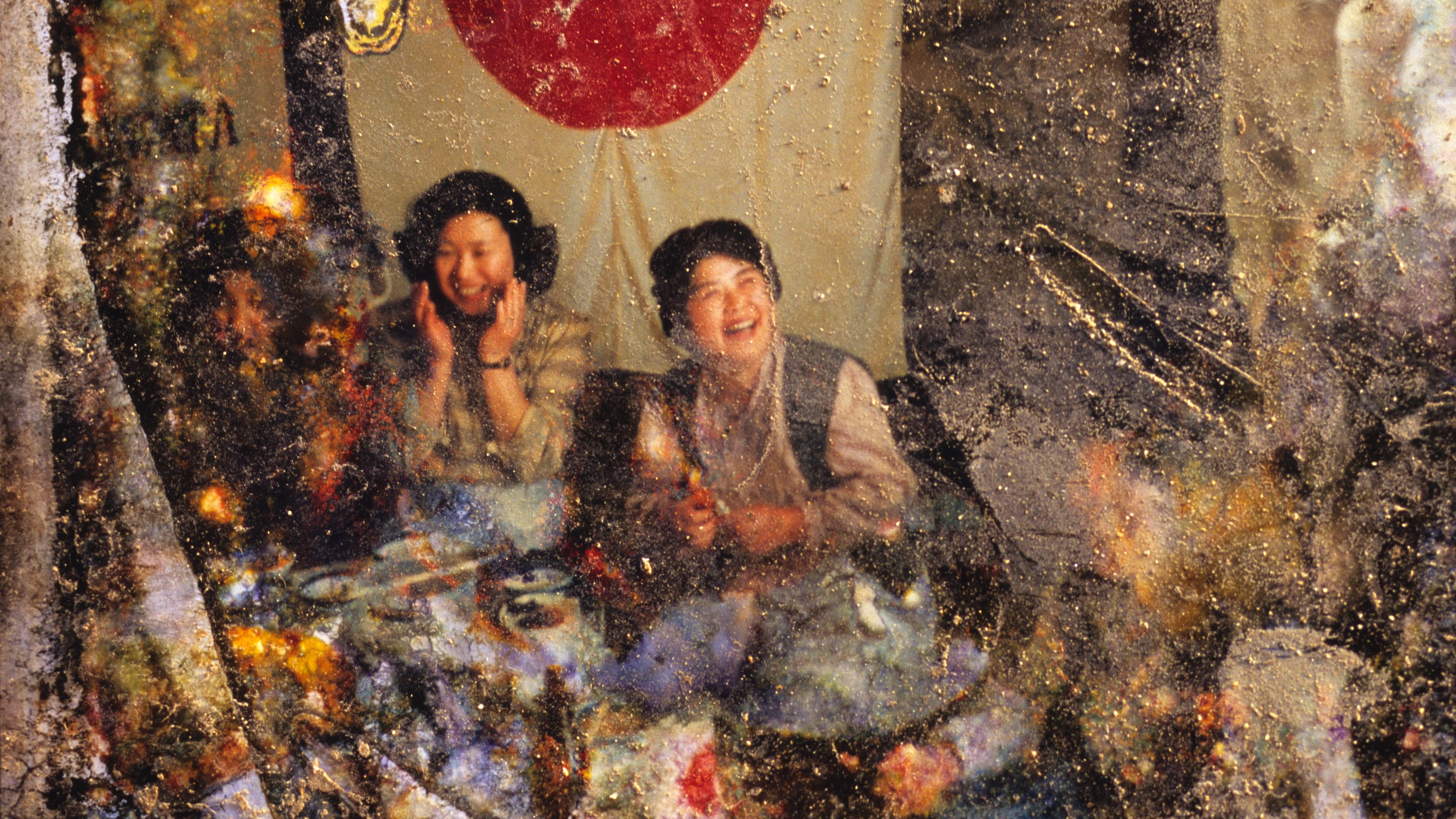 A damaged photo of people laughing at a table, with a large red circle on a banner in the background.