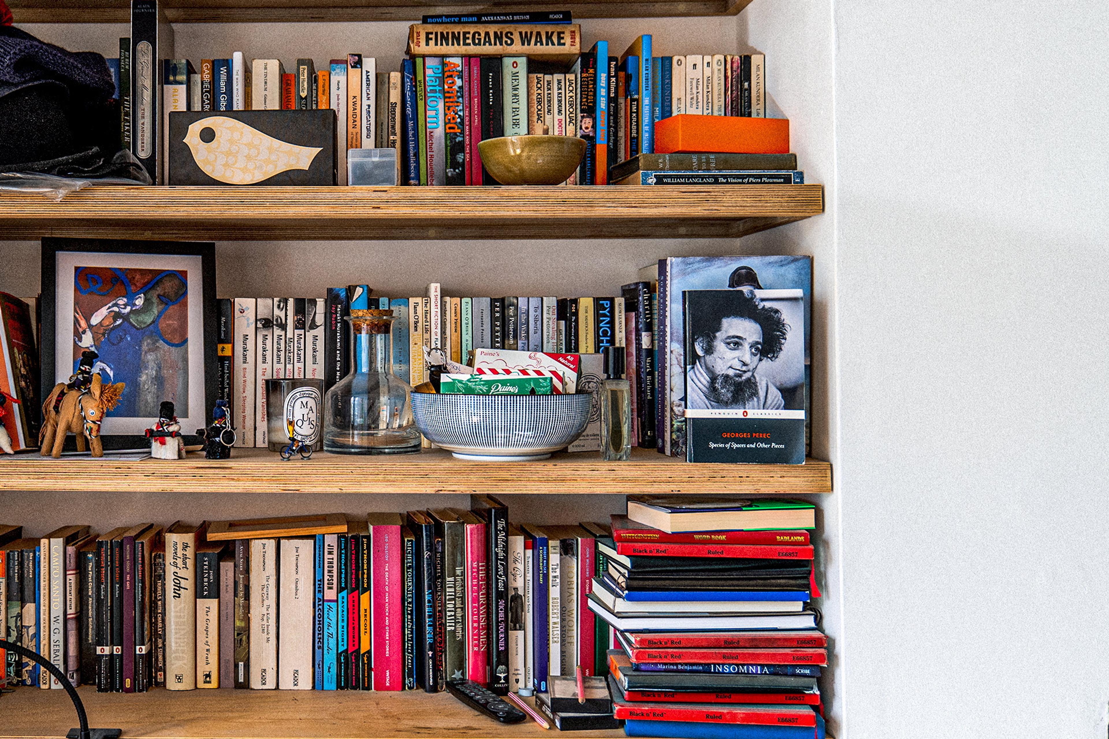 Photo of wooden bookshelves filled with books, small decor items and framed pictures in a cosy room setting.