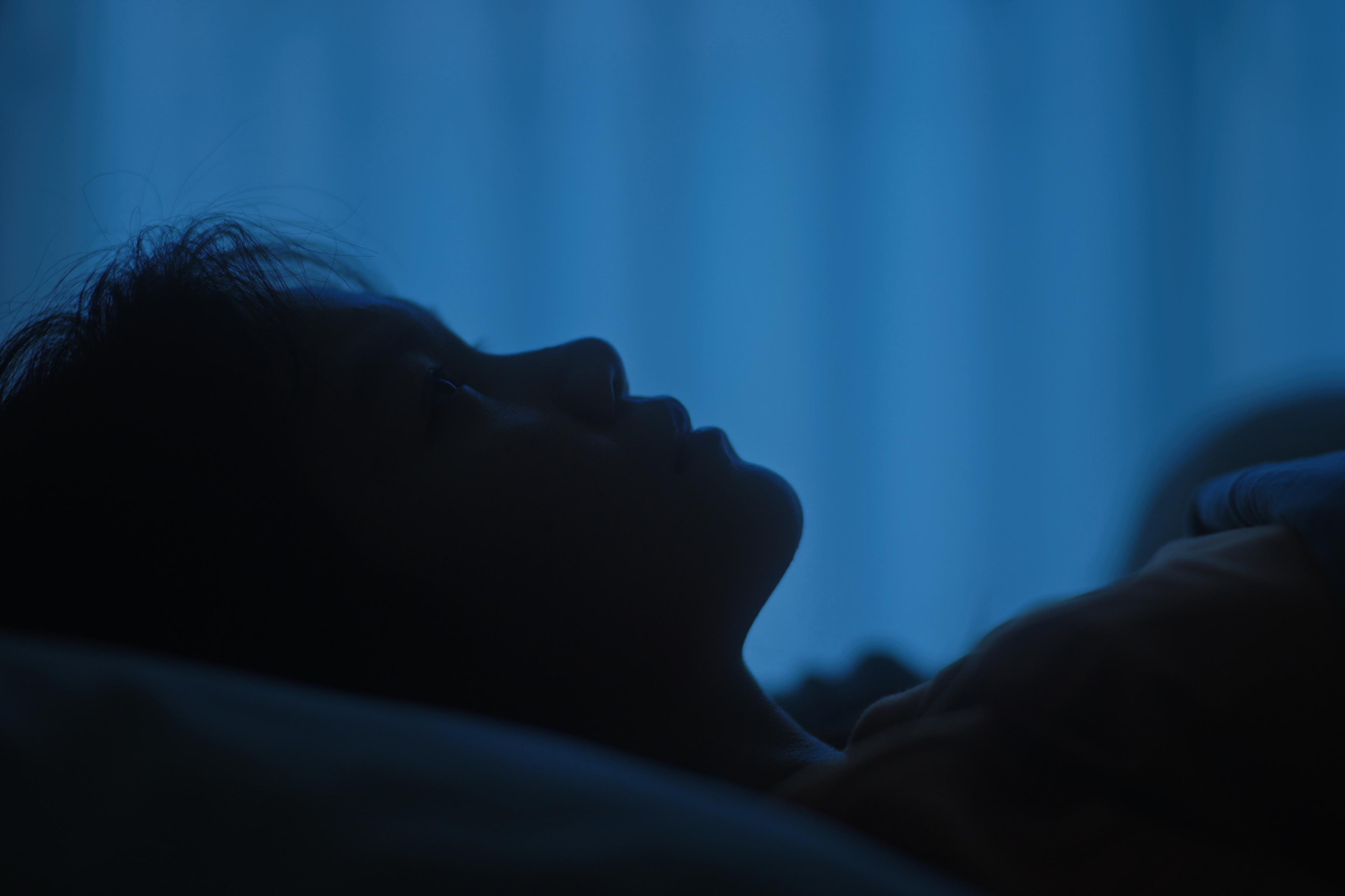 Photo of a person lying in profile in a dark room with blue light, showing a calm expression and dim surroundings.