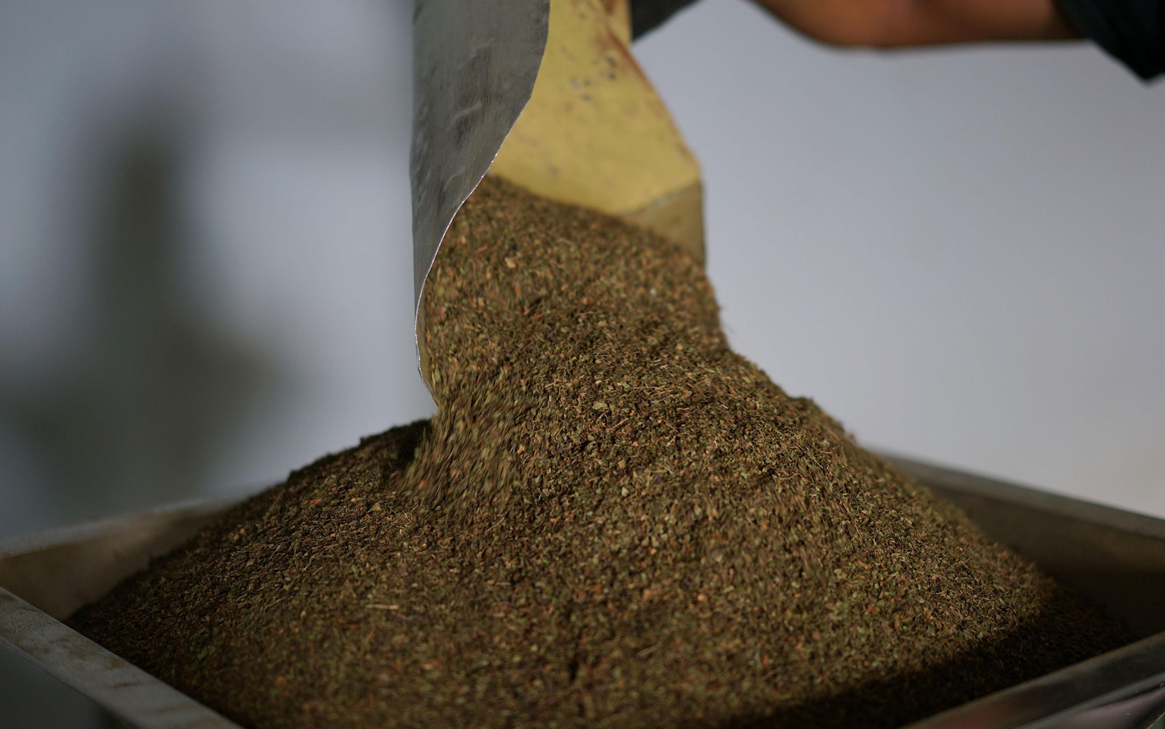 Dried ground leaves being poured from a scoop into a container indoors.