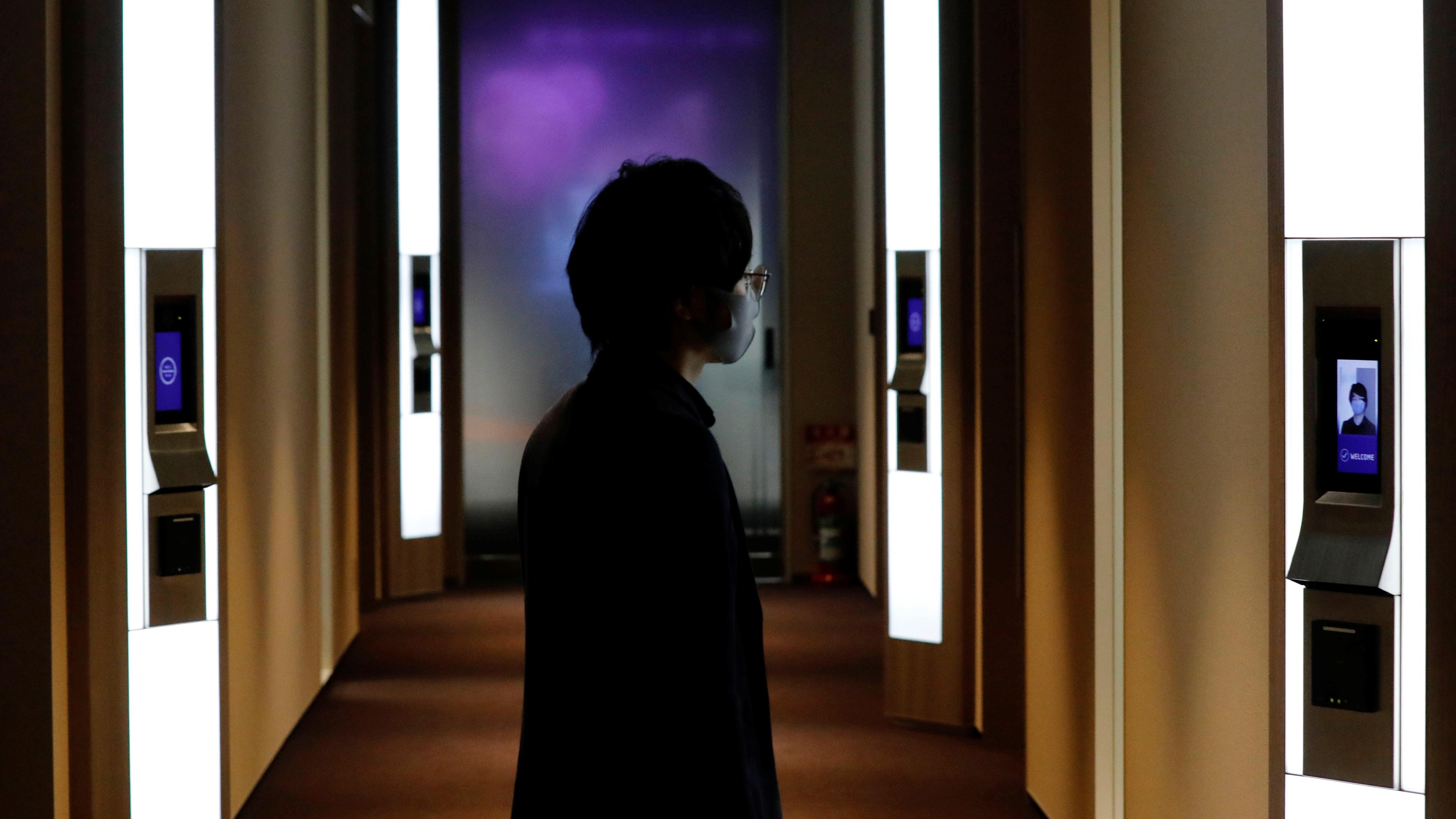 Photo of a person using facial recognition in a dimly lit hallway with illuminated screens on the walls.