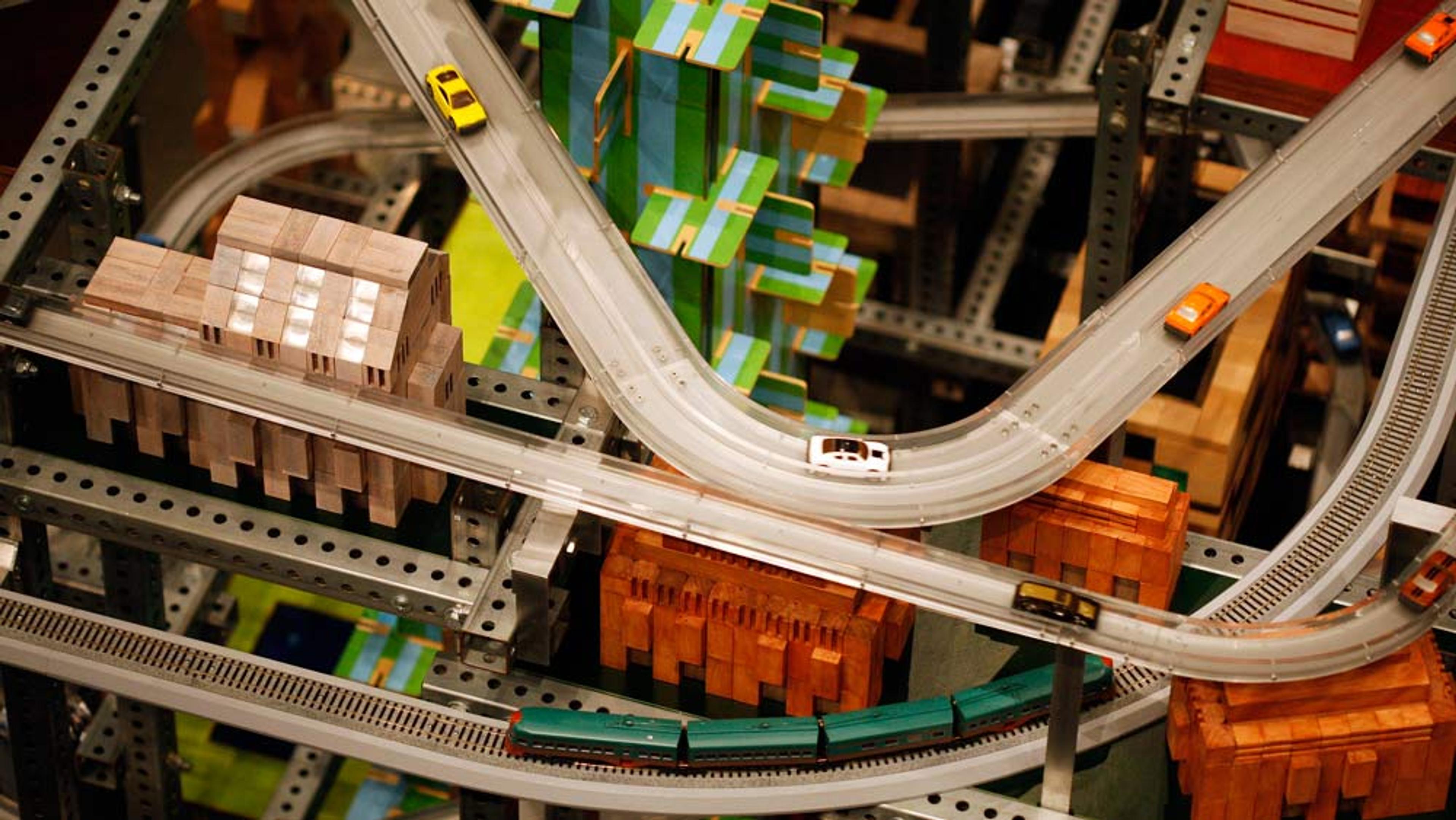 A detailed toy city model with elevated roads, colourful buildings, small cars, and a train track below.