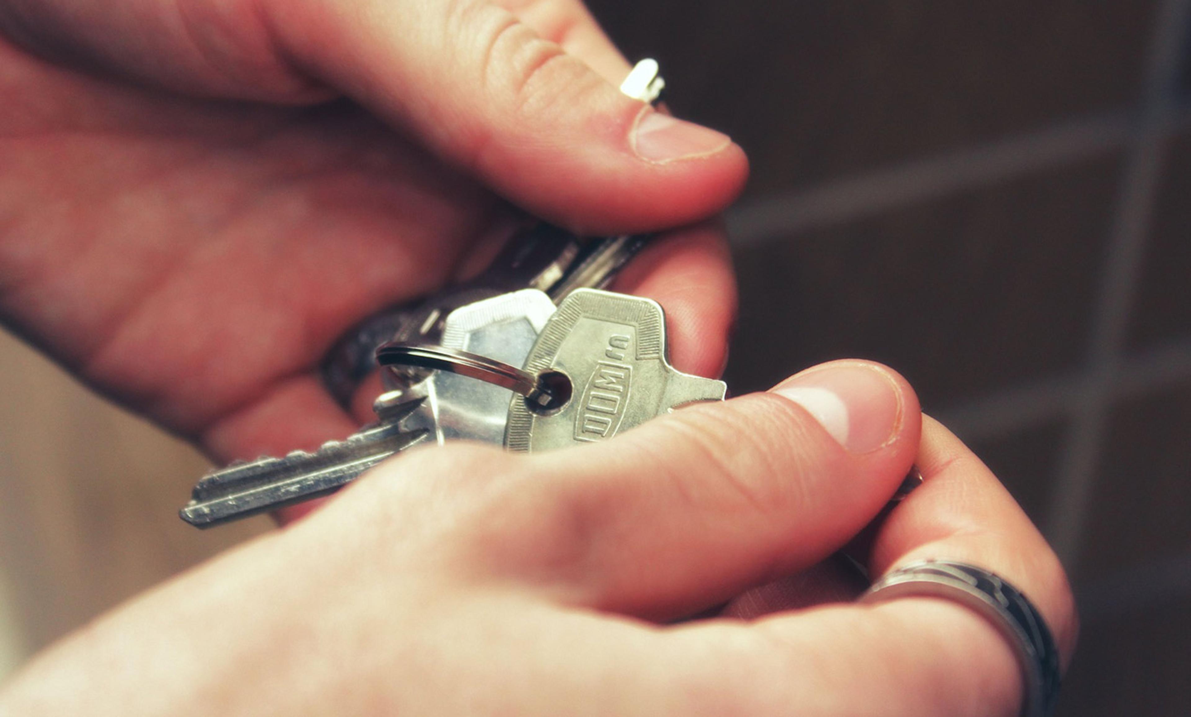Hands holding a set of metallic keys. A keyring with multiple keys is shown, and the fingers are slightly focused.