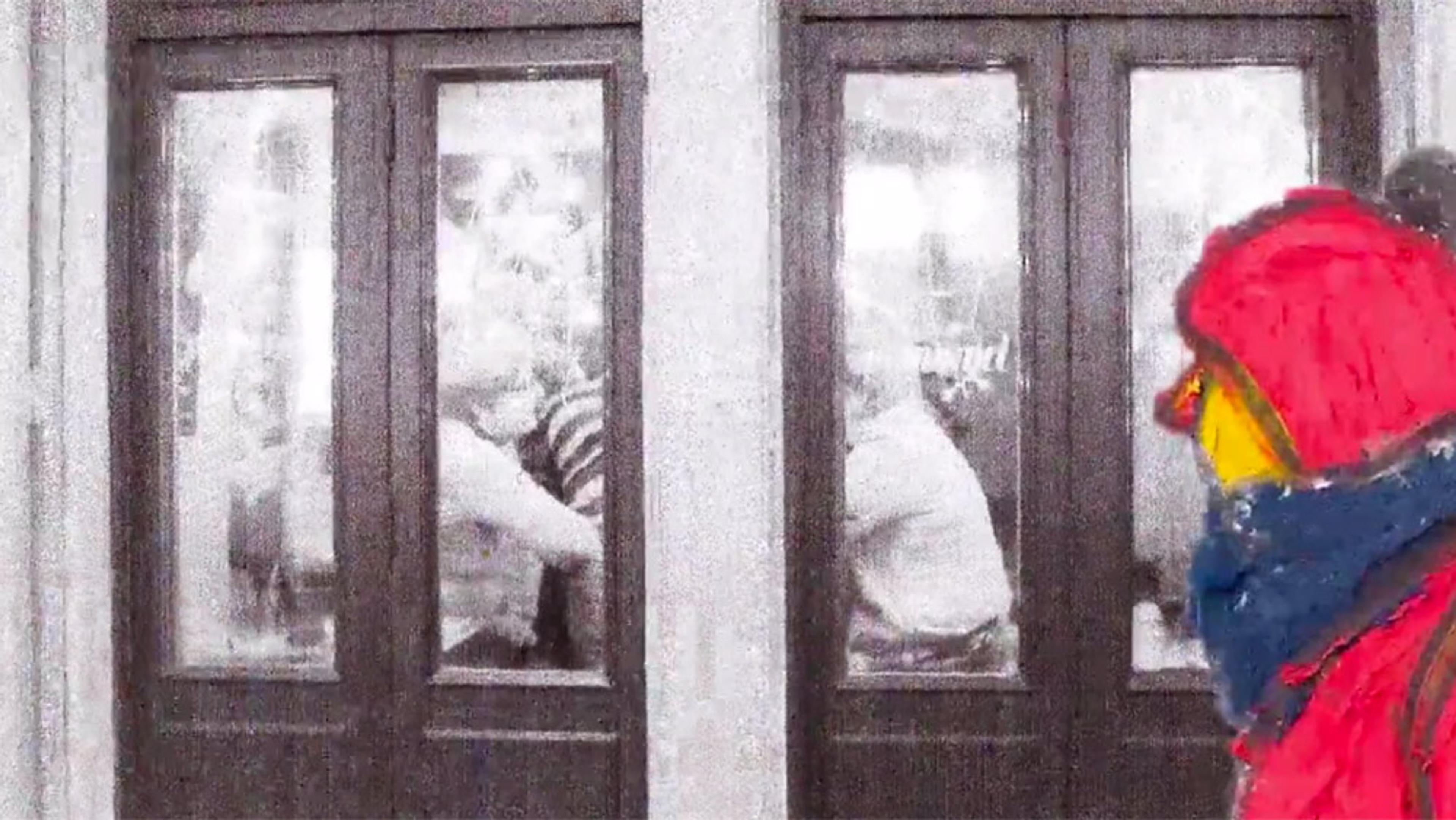 Painting of a person in a red jacket standing outside a glass door with multiple people visible through the glass indoors.