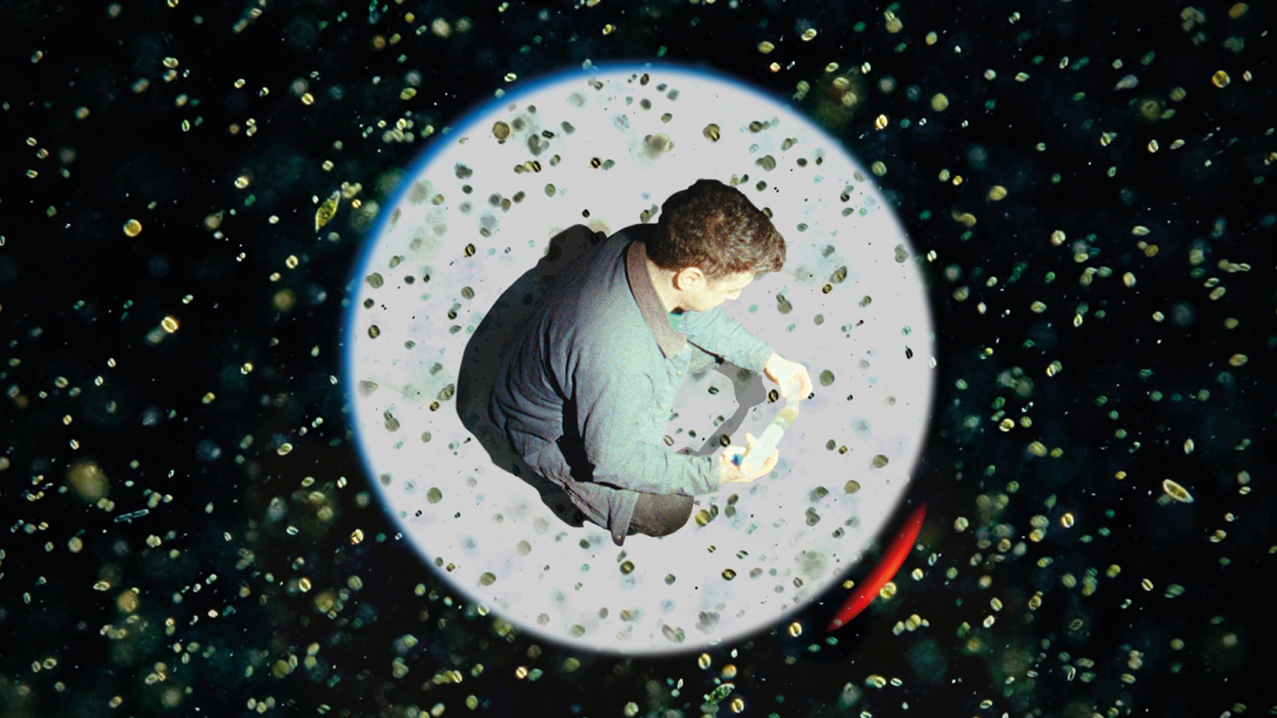 Photo of a man sitting in a circle on a speckled background, focusing on an object in his hands, with a cosmic effect.