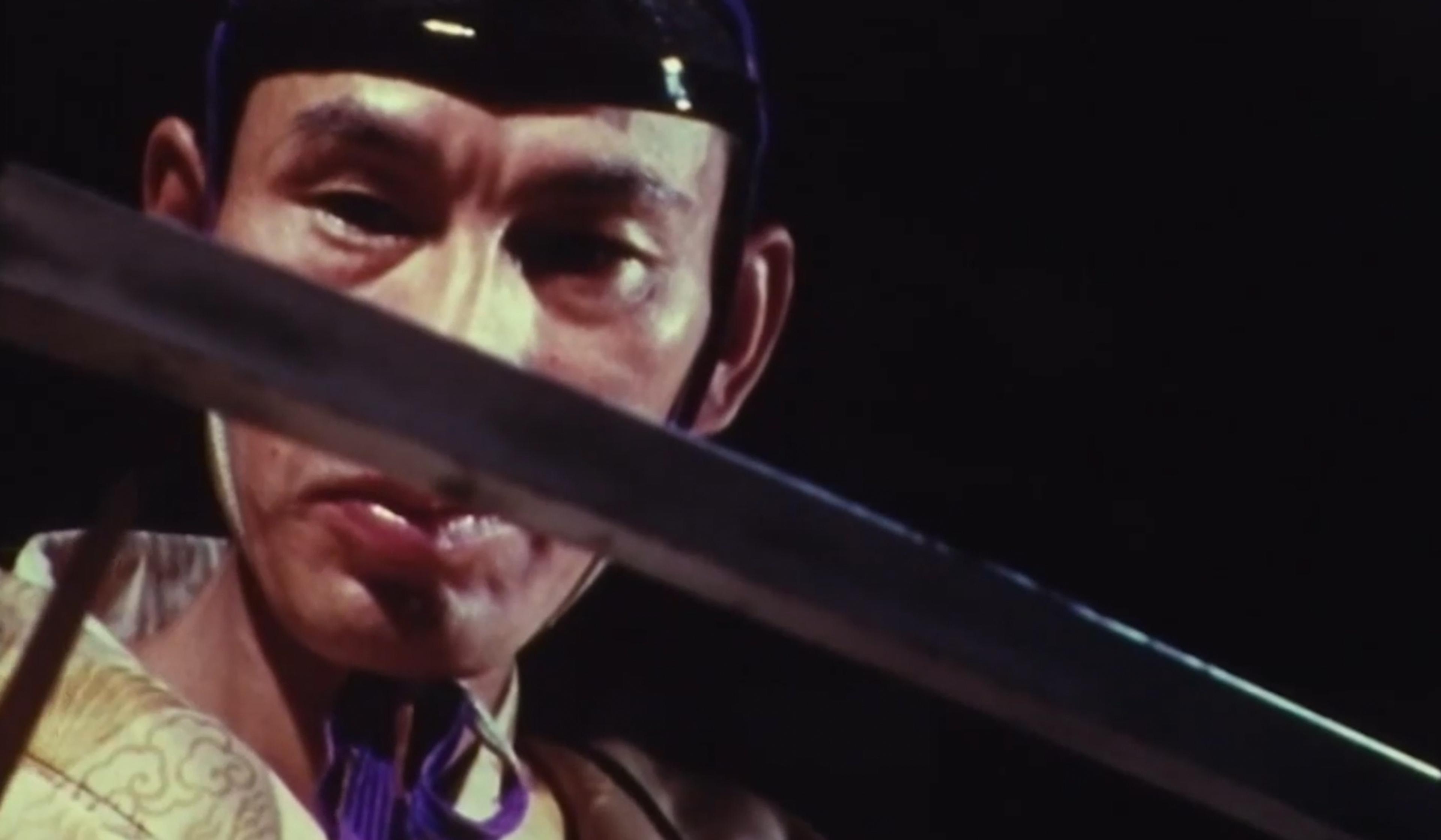 Close-up of a person holding a sword, focusing intently. The background is dark, highlighting the facial expression and the blade.