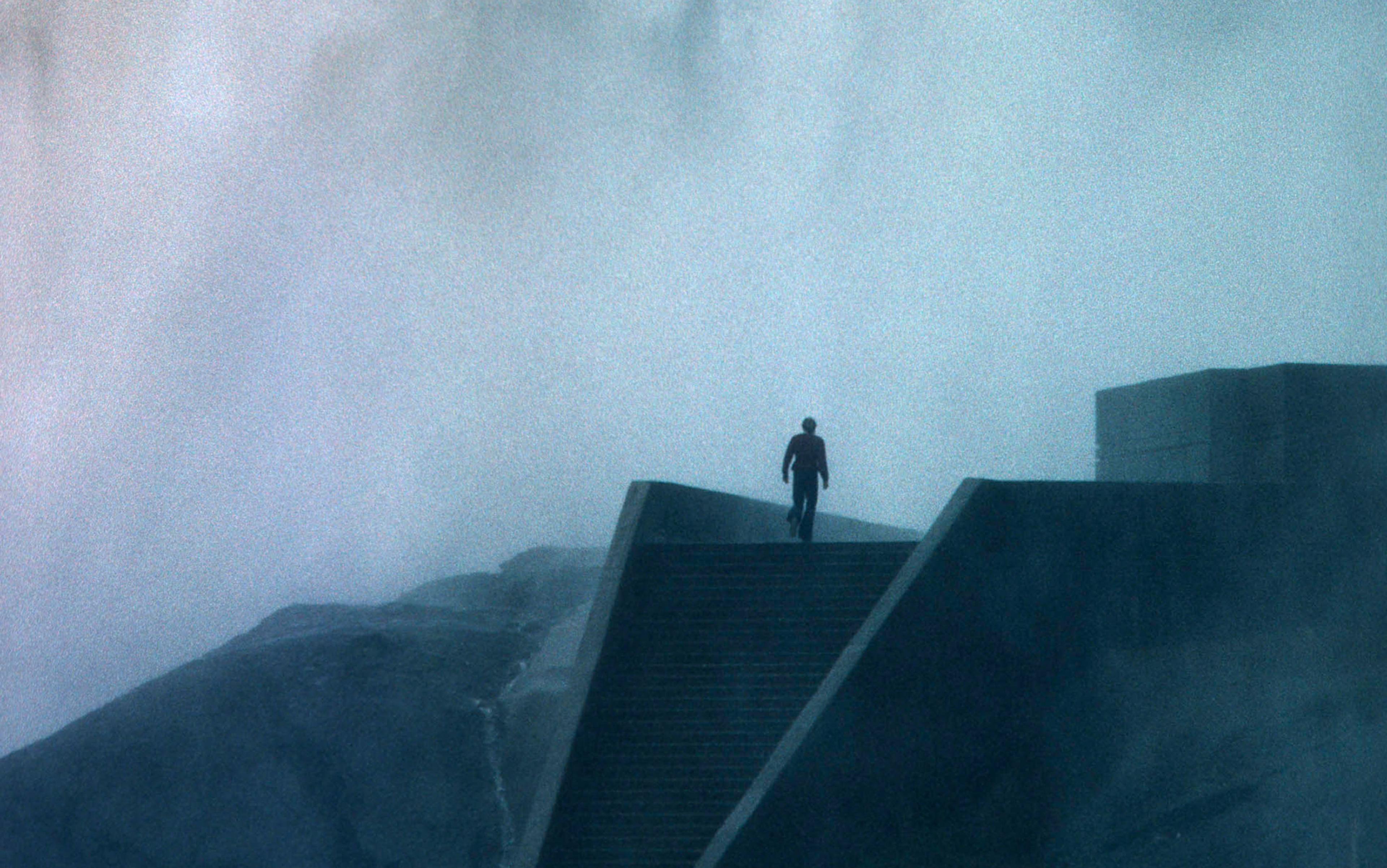 A solitary figure walking up misty stairs toward an unclear building, creating a mysterious atmosphere.