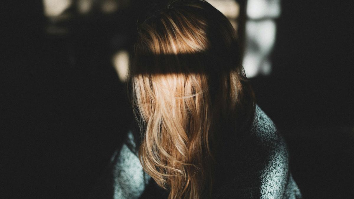 A person with long blonde hair covering they’re face in shadowy light.
